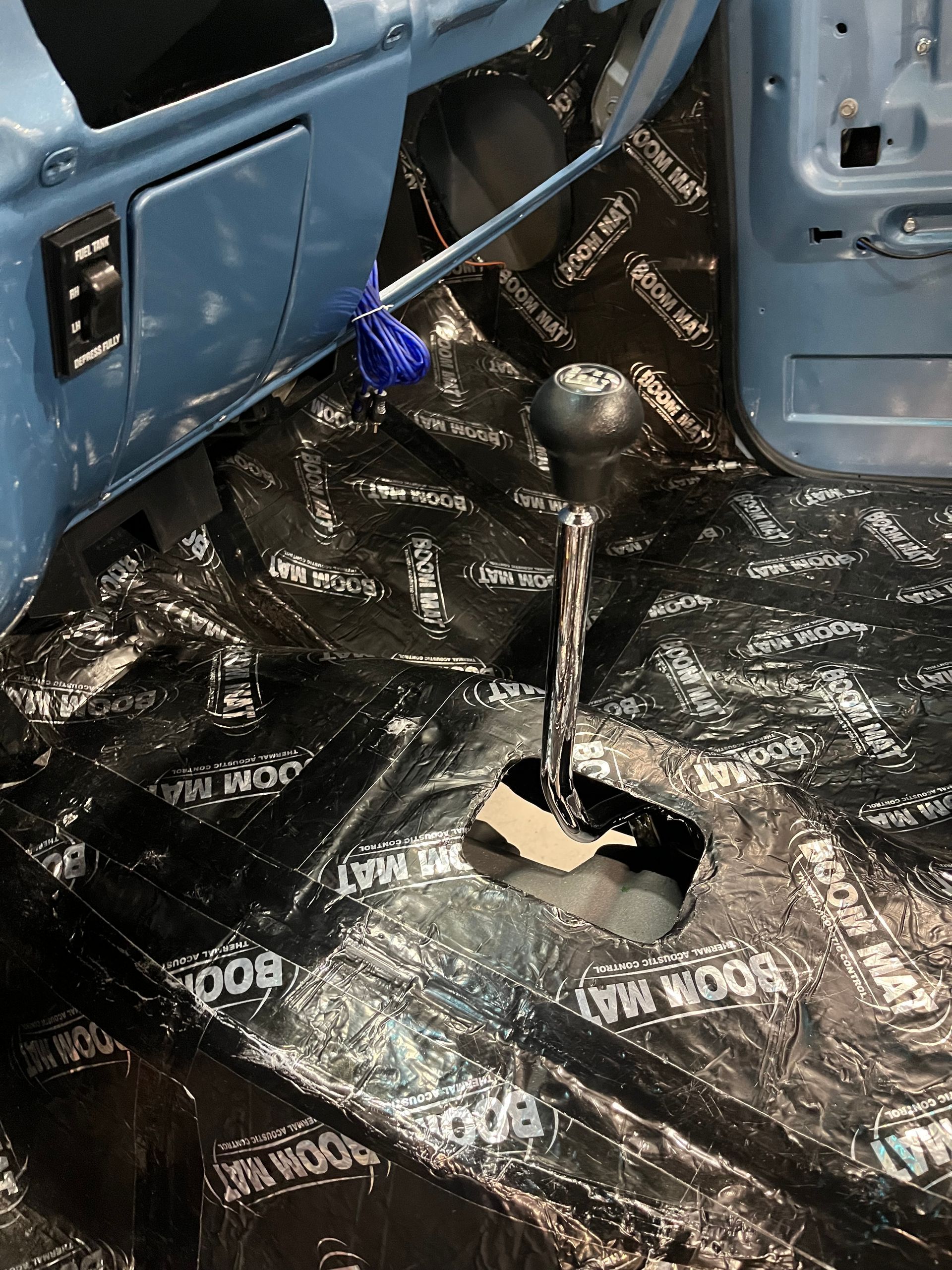 Car interior with exposed floor, loose gear shifter, and black soundproofing material covering the floor.