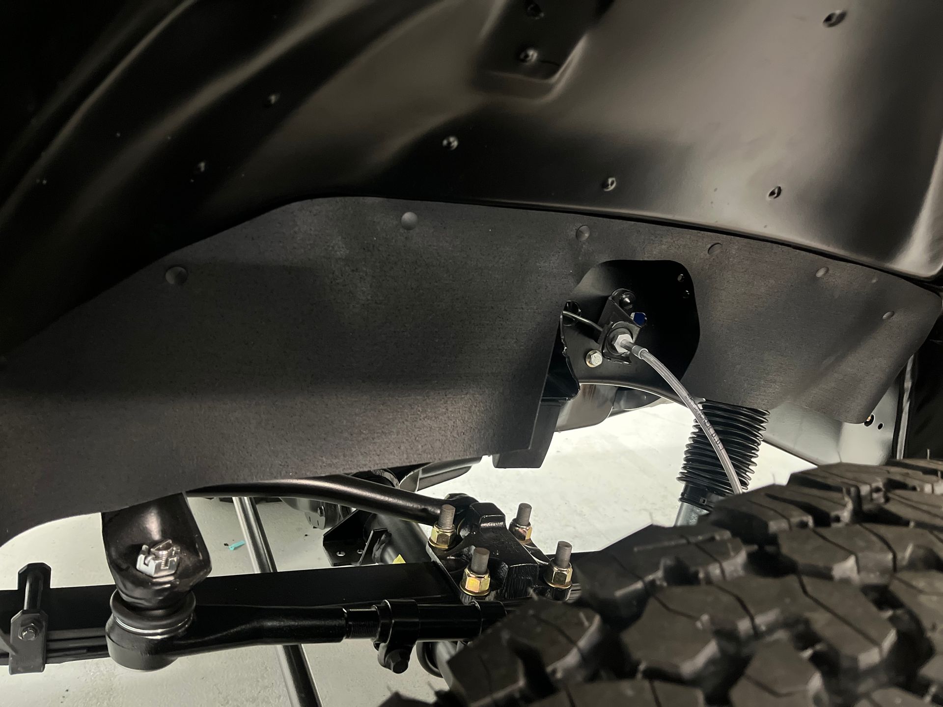 Close-up of a black vehicle wheel well and suspension above a rugged tire