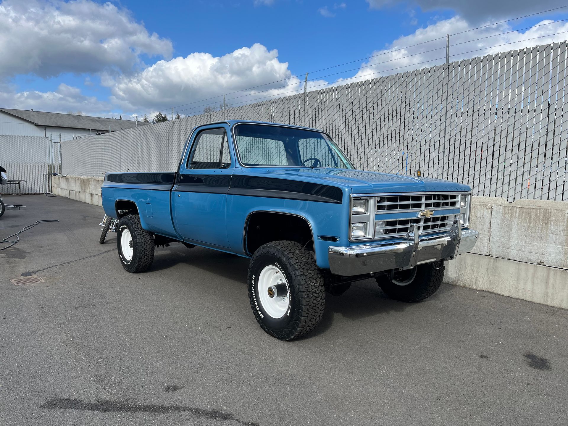 Blue vintage pickup truck parked by a concrete wall under a partly cloudy sky