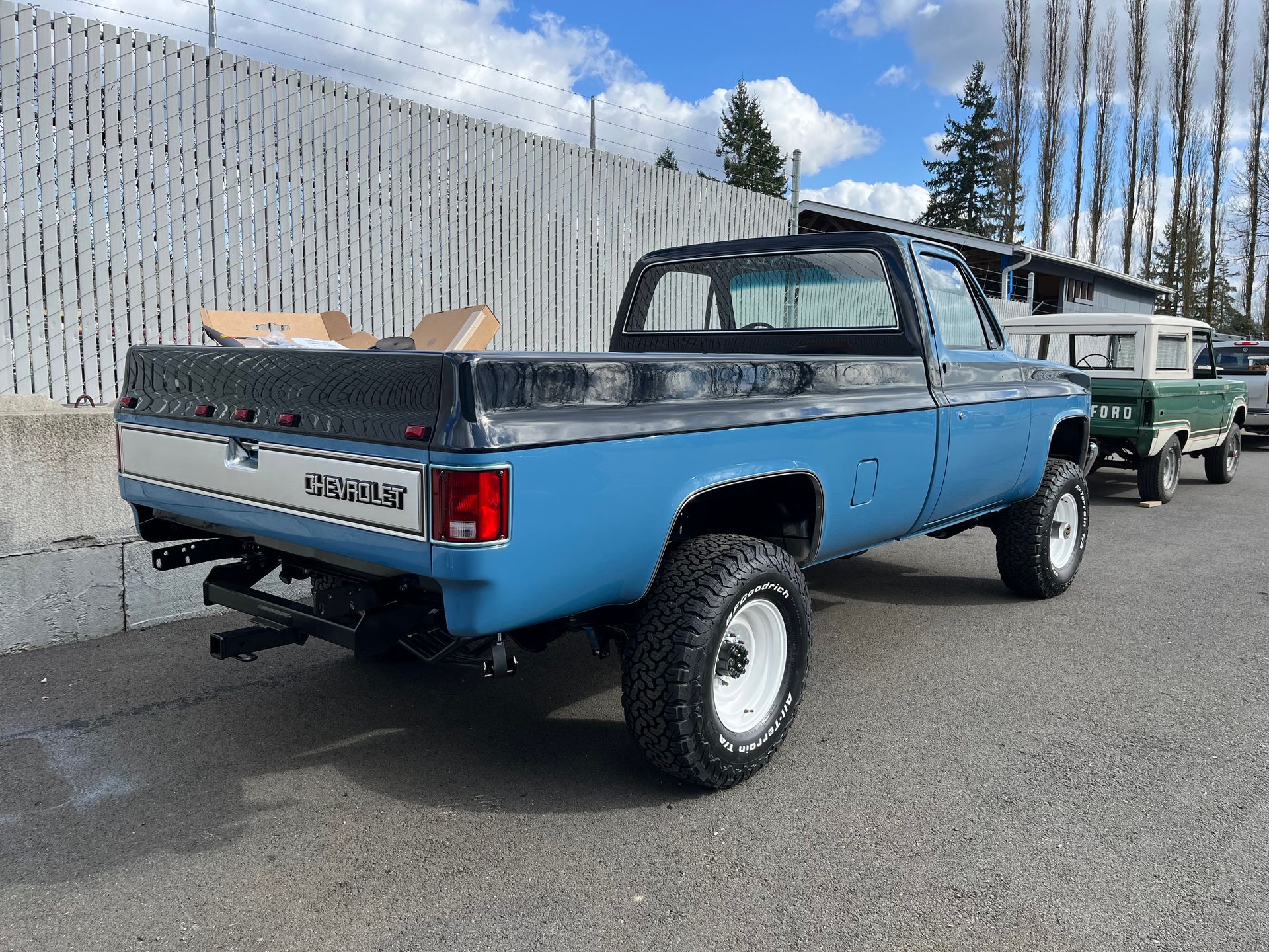 Blue lifted pickup truck parked outdoors beside a fence.