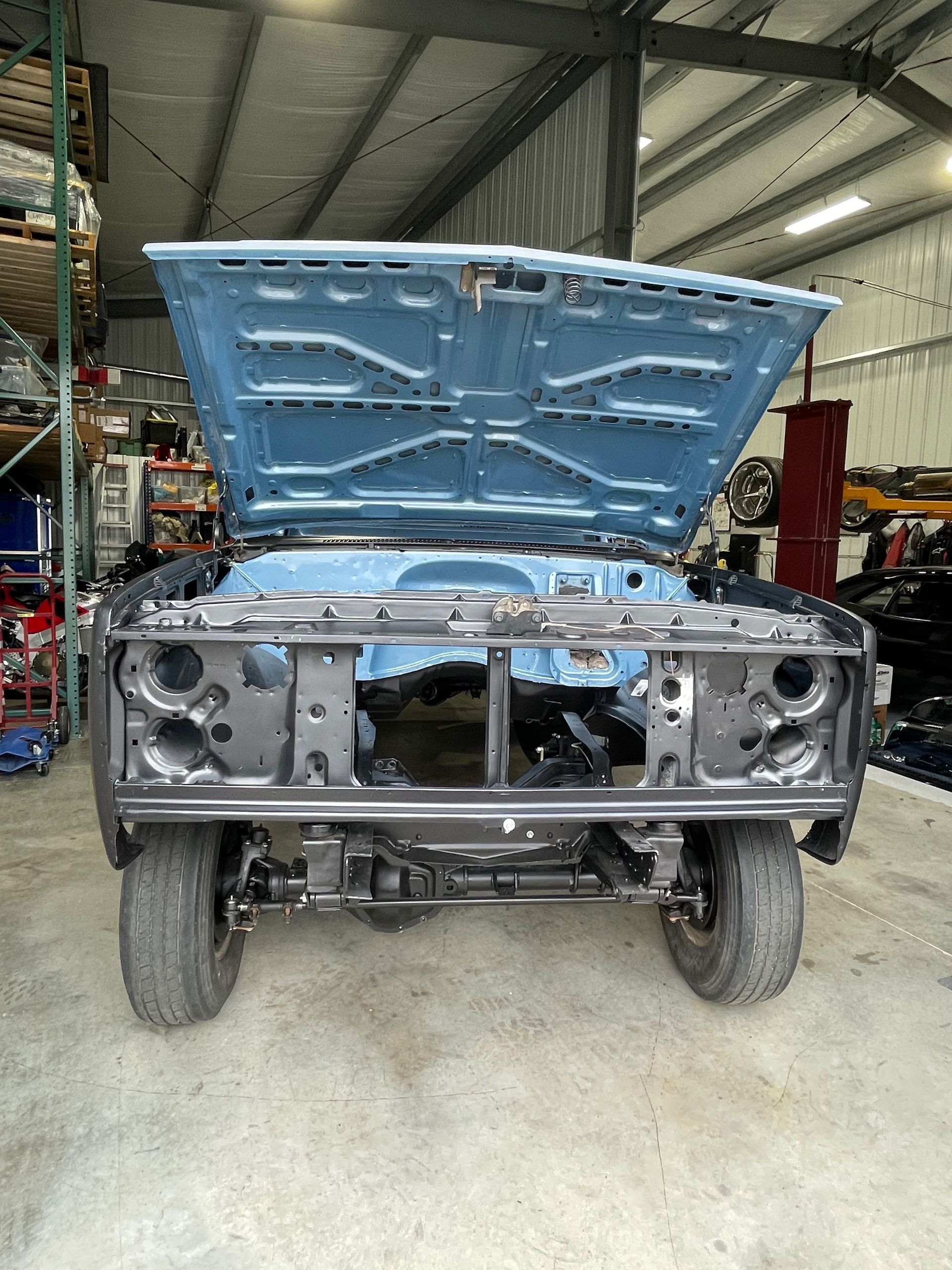 Front view of a partially restored truck in a garage, with the blue hood open and the front grille removed.