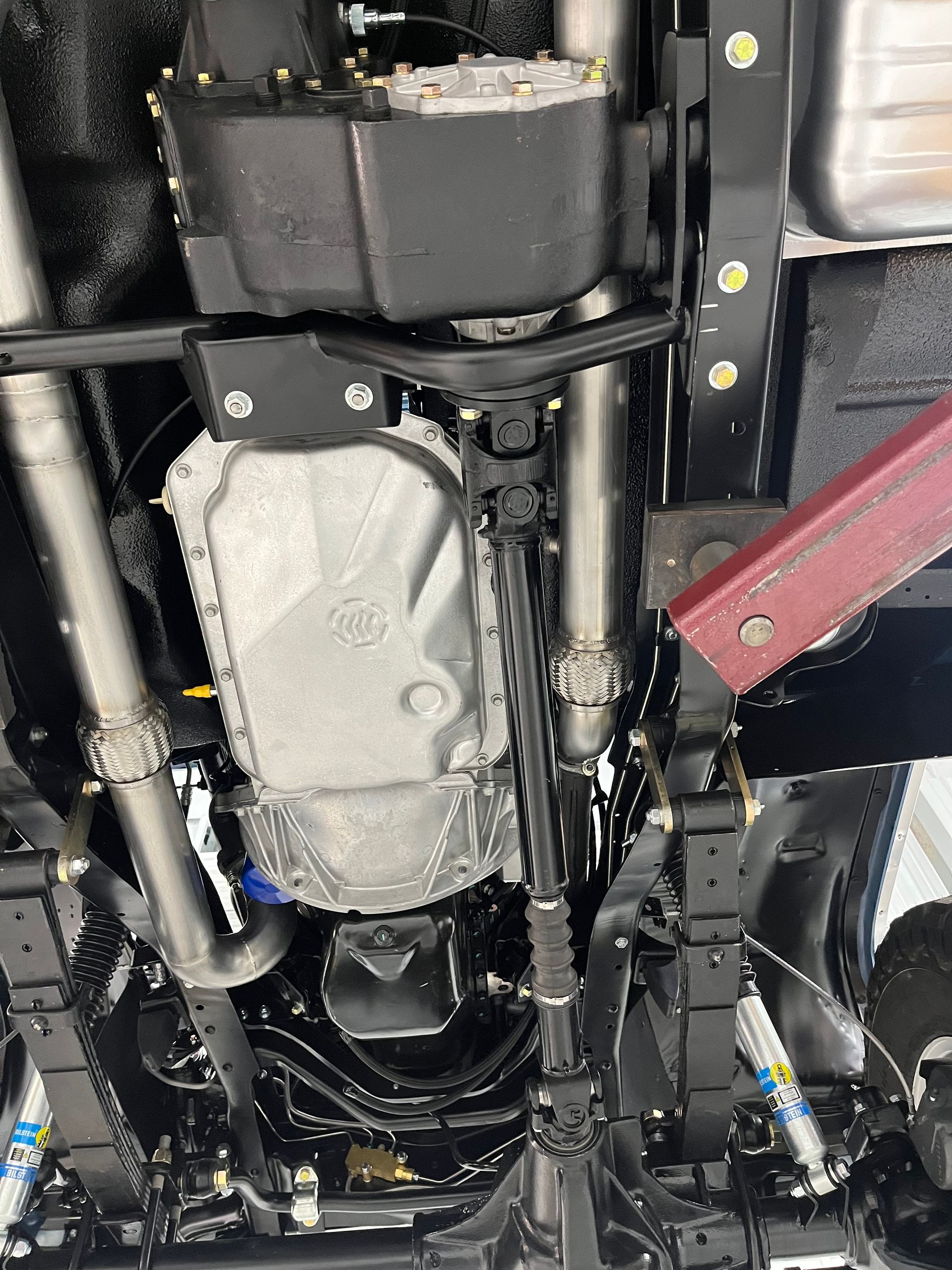 Undercarriage view of a vehicle showing exhaust and drivetrain components with a red suspension arm.