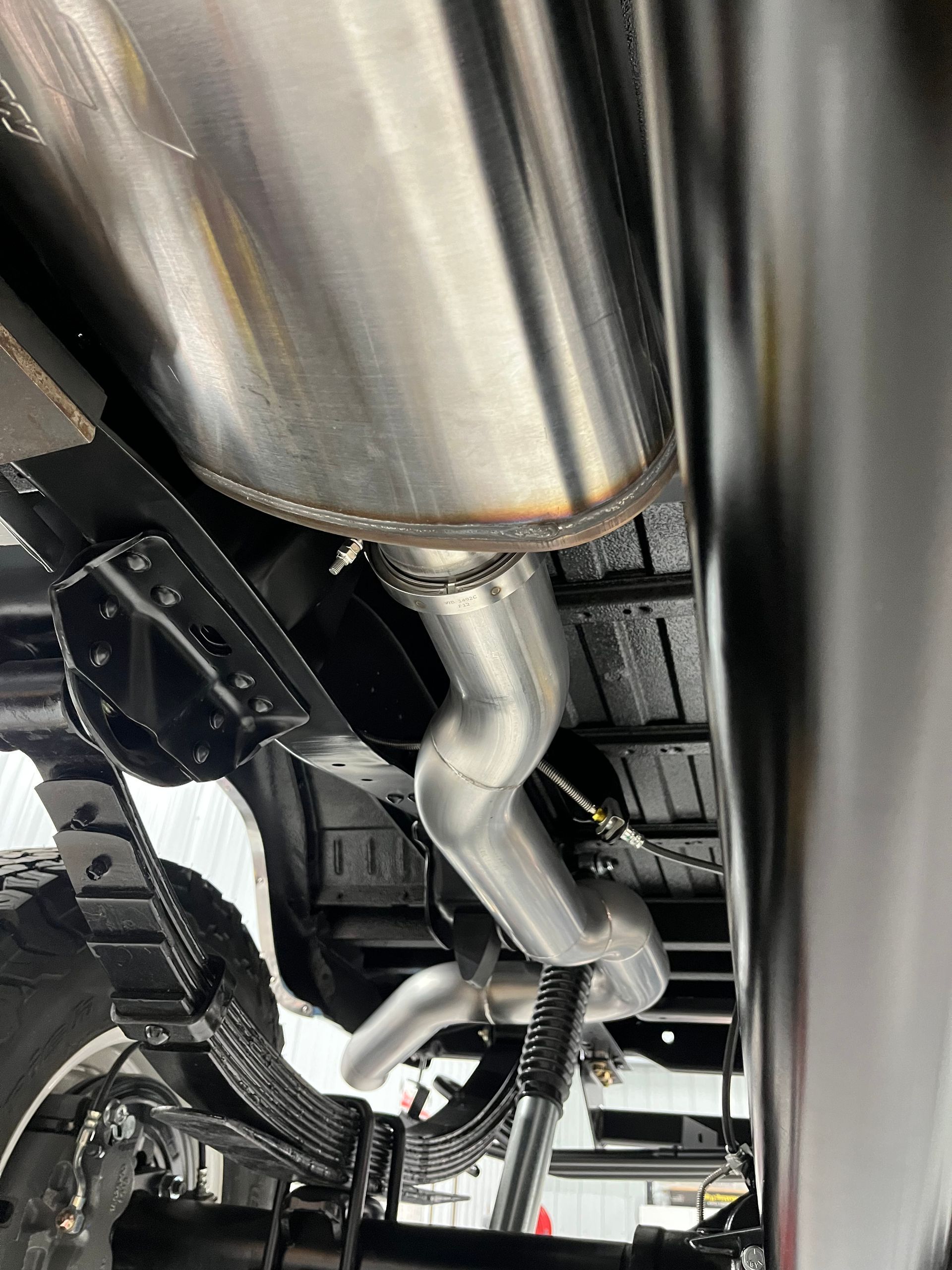 Undercarriage view of a vehicle with shiny exhaust pipes and suspension components on a lift