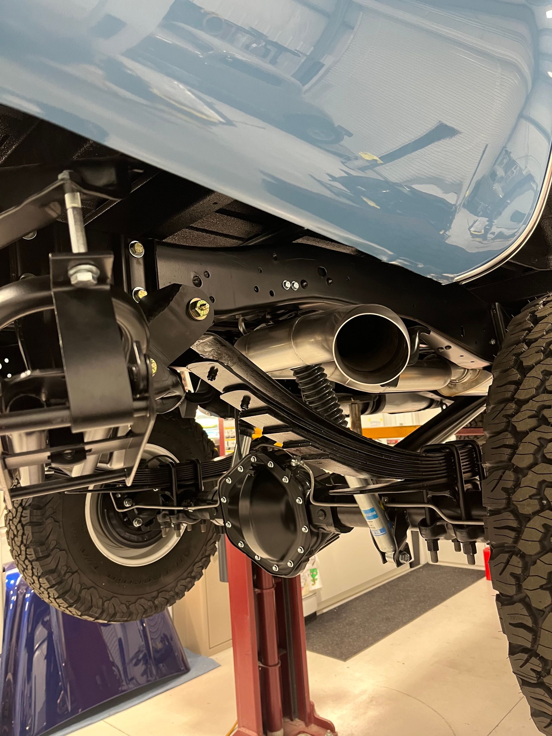 Underbody view of a blue off-road vehicle on a lift, showing large tires and suspension components