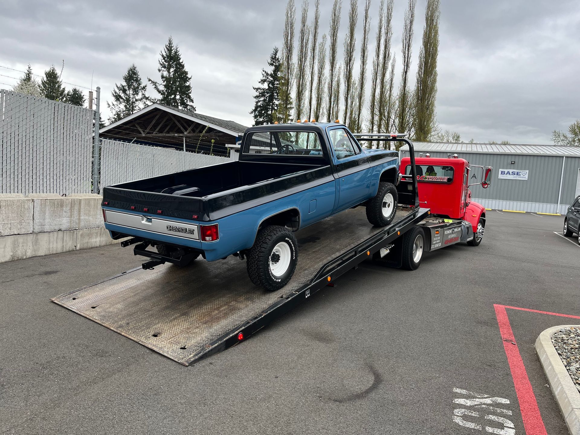 Blue pickup truck loaded on a tow truck ramp in a parking lot