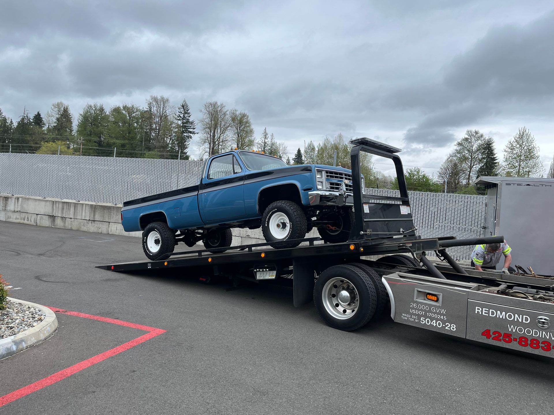 Blue classic car on a flatbed tow truck in a parking lot under cloudy skies
