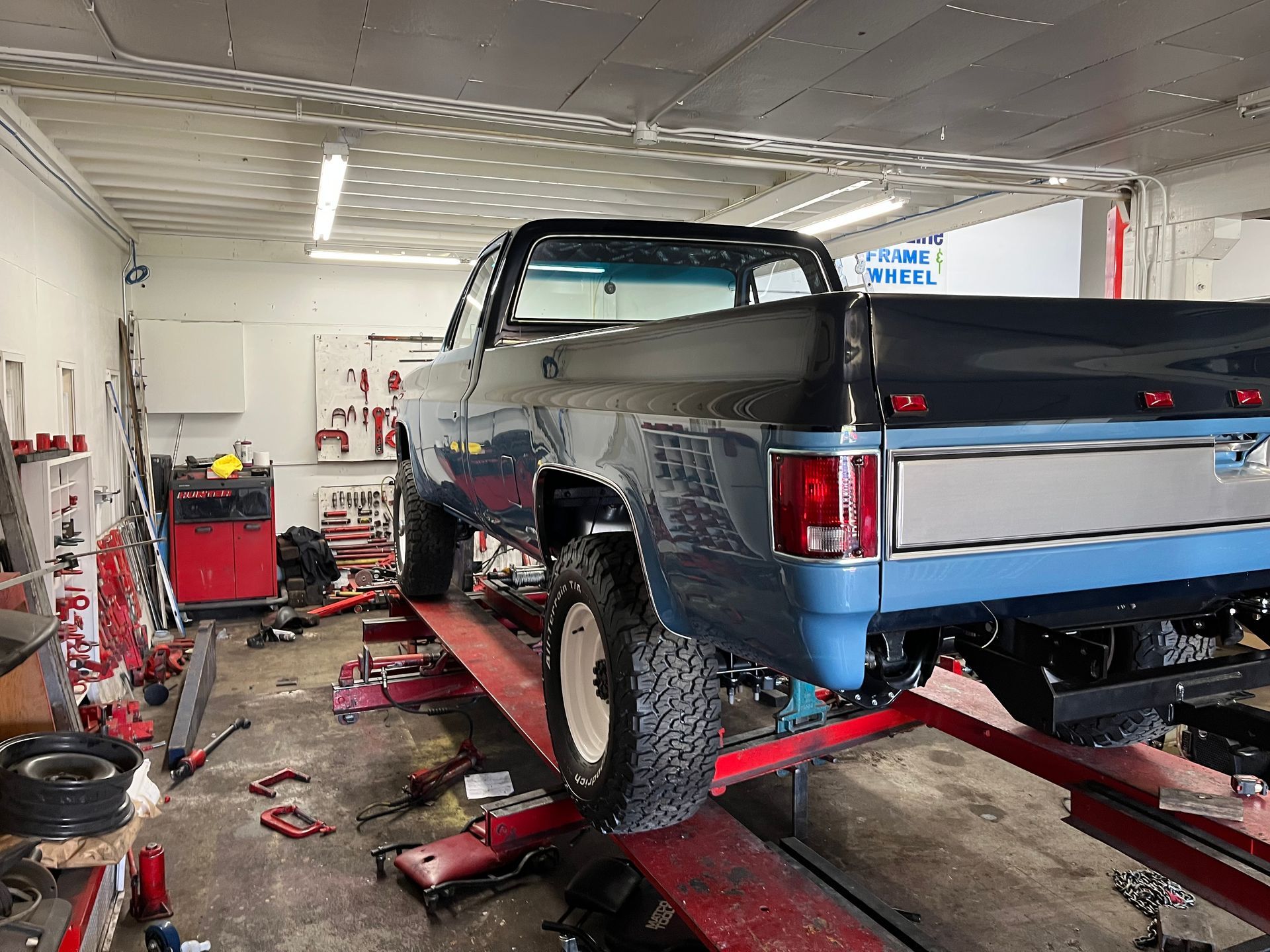 Blue pickup truck raised on a lift in an auto repair shop with tools and equipment around it