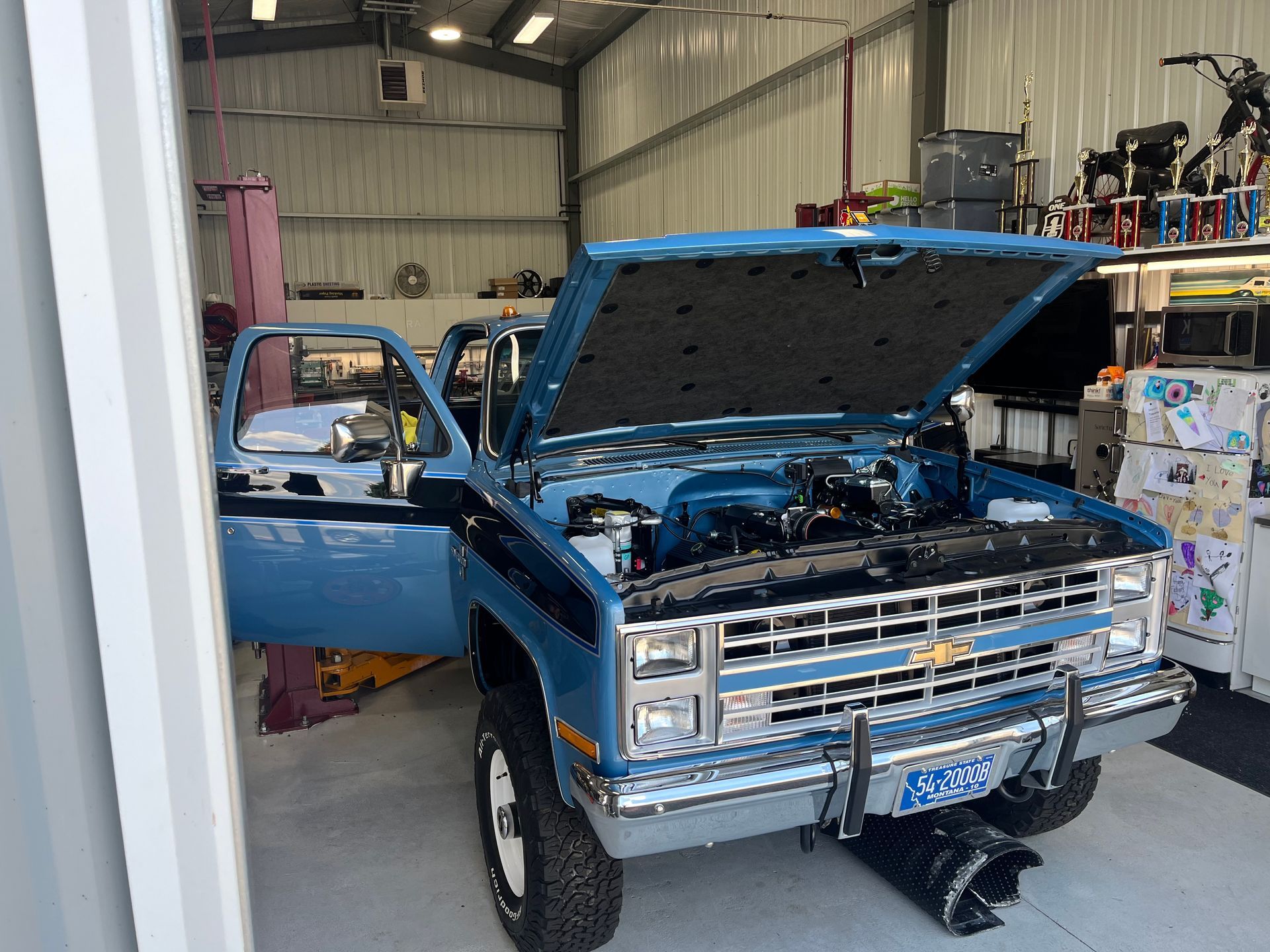 Blue pickup truck with open hood and driver door in a workshop garage