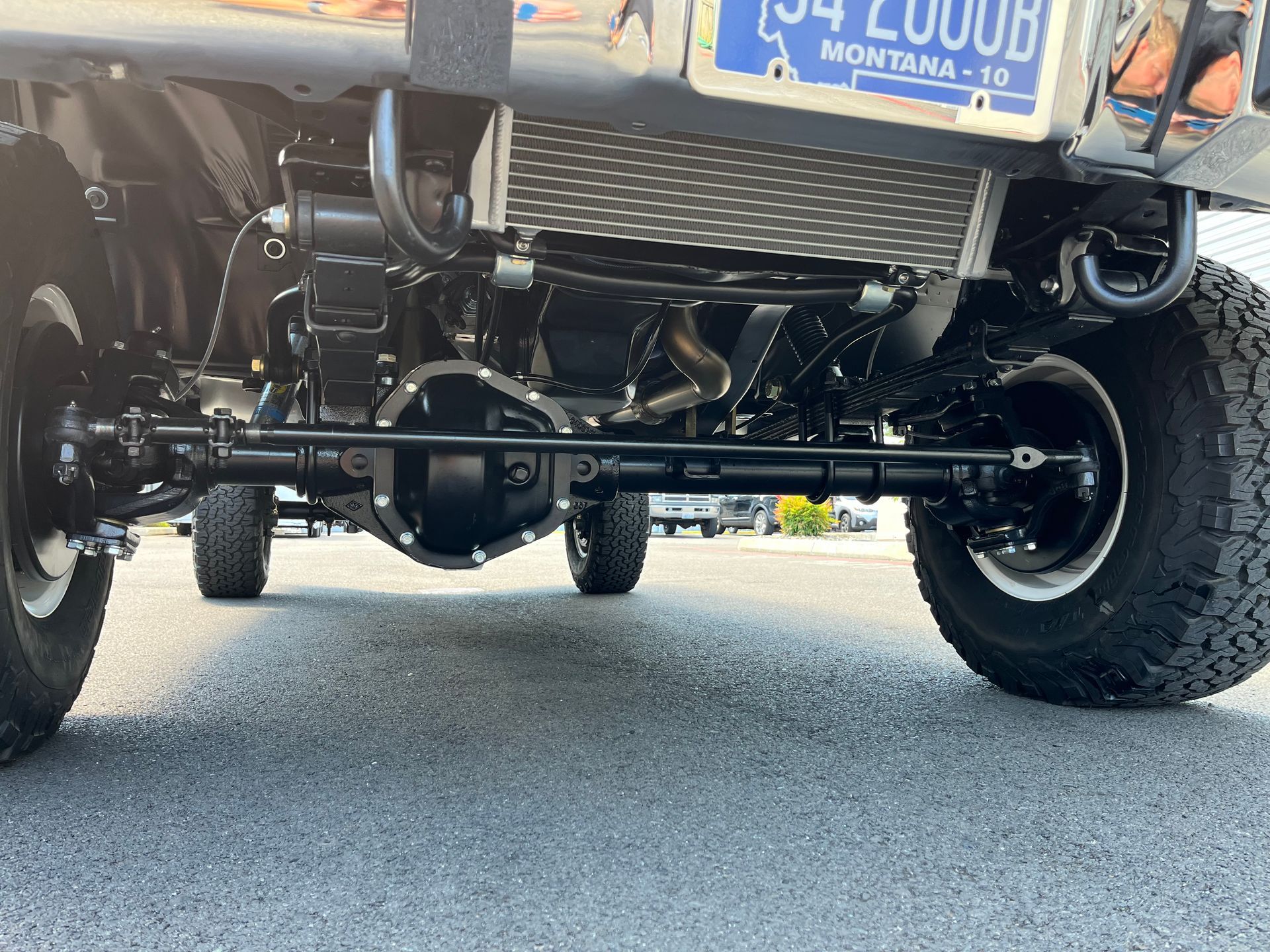 Underneath view of a lifted truck’s rear suspension and differential on a road, with a blue Montana plate visible