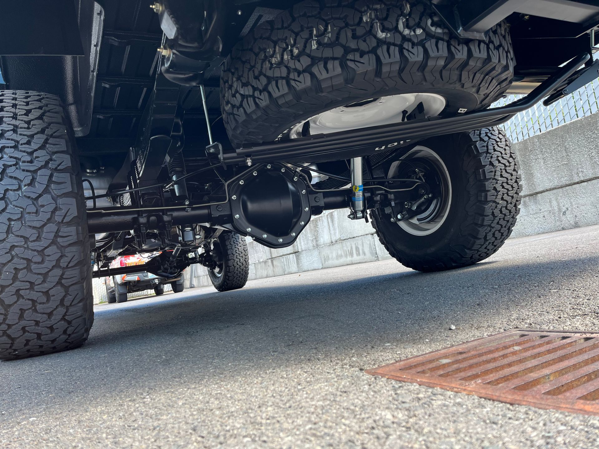 Underneath view of a lifted off-road truck with large tires on a paved street.