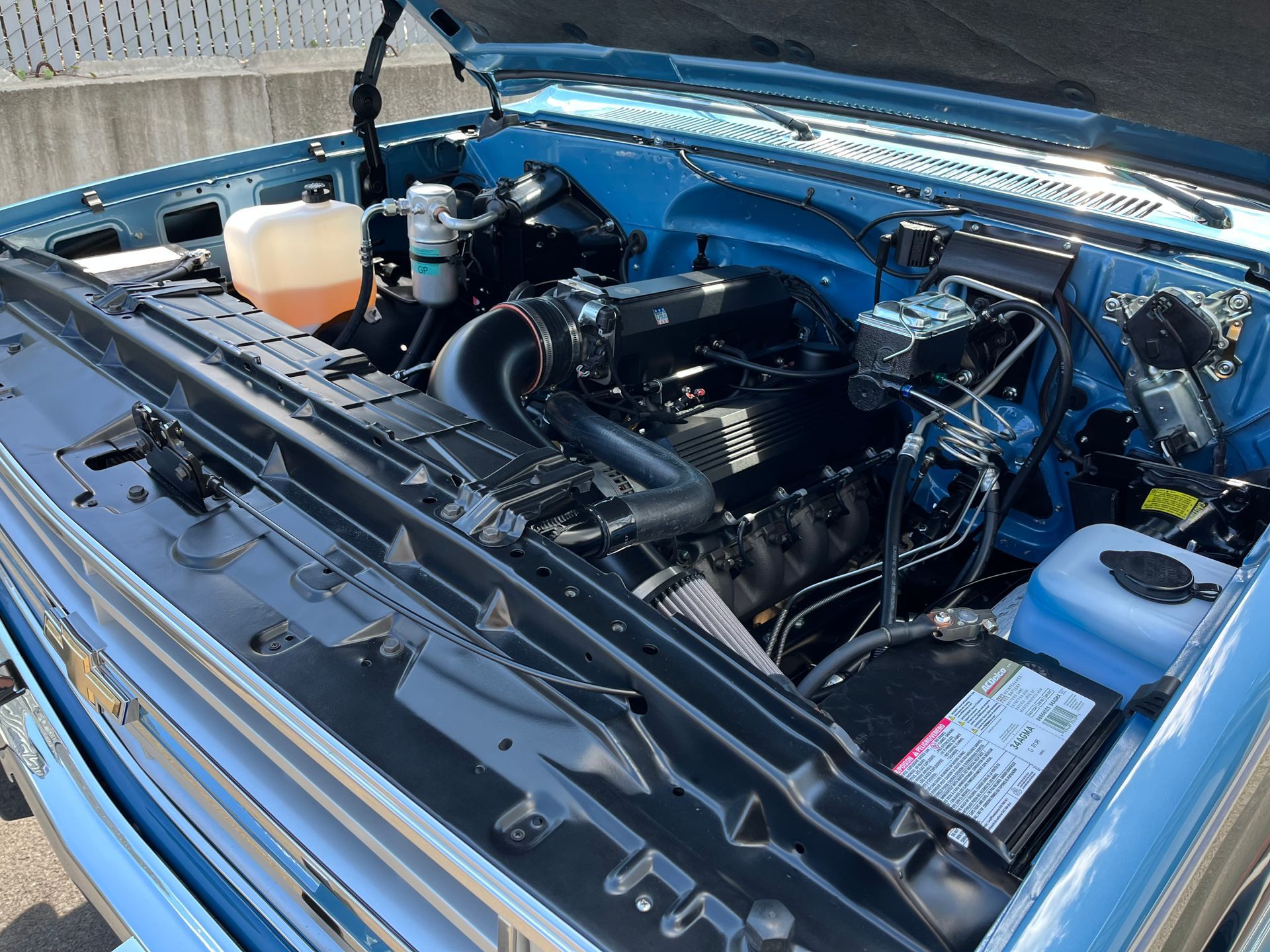 Open truck engine bay with blue bodywork and visible hoses, battery, and fluid reservoir