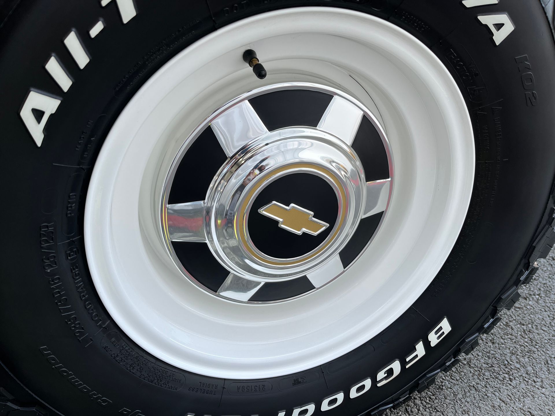 Close-up of a white car wheel with a chrome hubcap and gold emblem, black tire visible