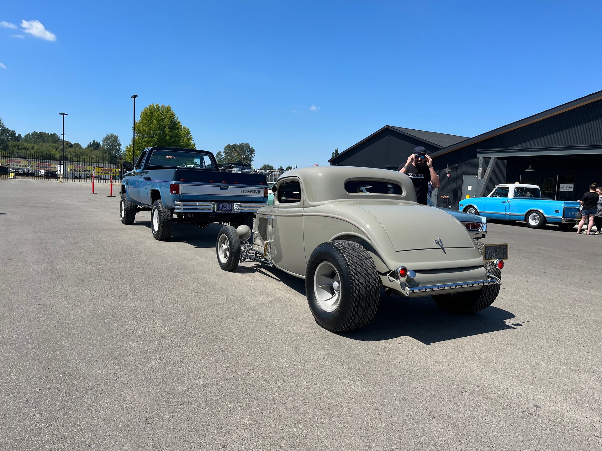 Two classic hot rods parked on an asphalt lot outside a building on a sunny day