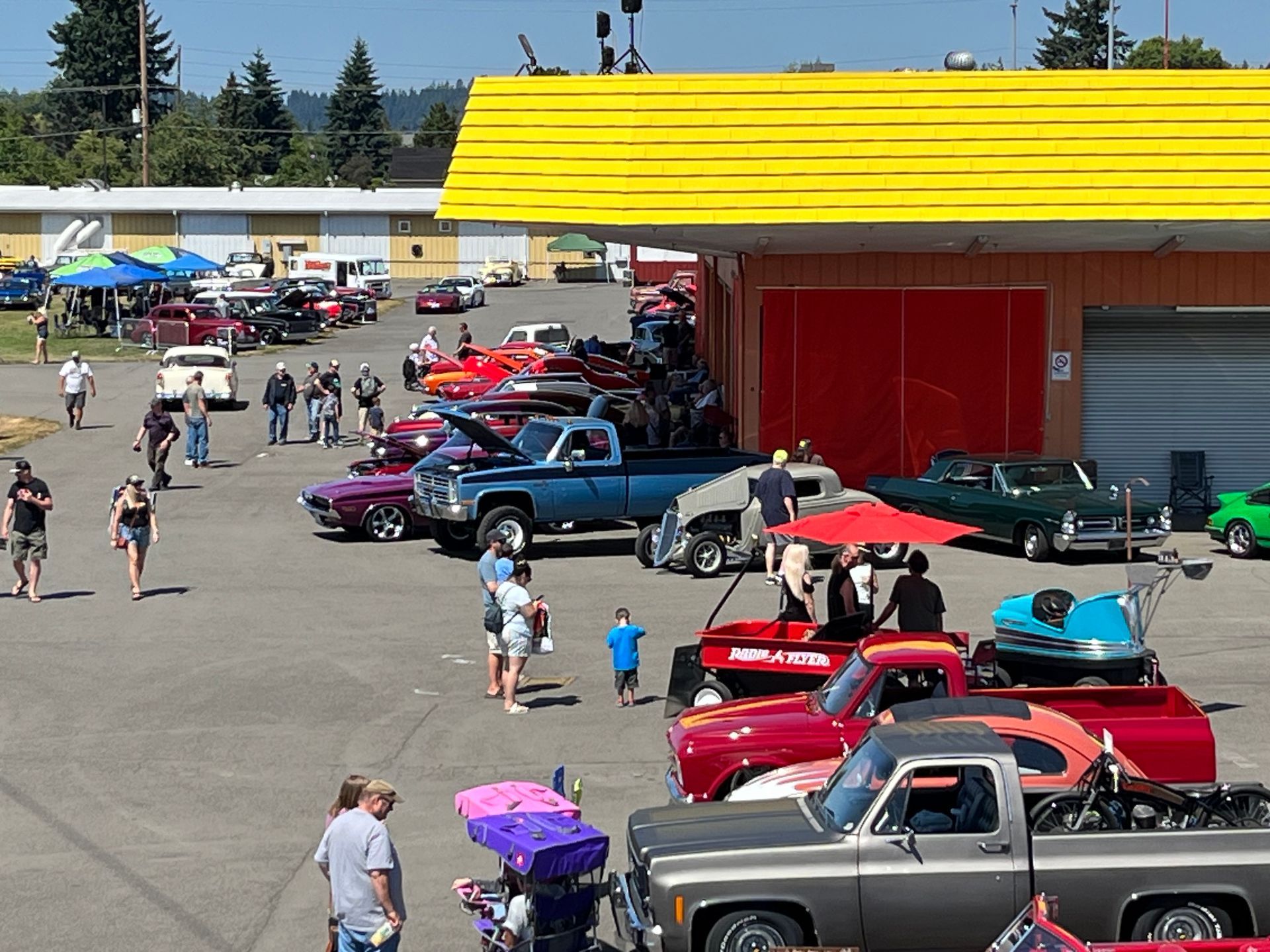 Classic car show with colorful vintage vehicles parked in rows beside a yellow-roofed building outdoors