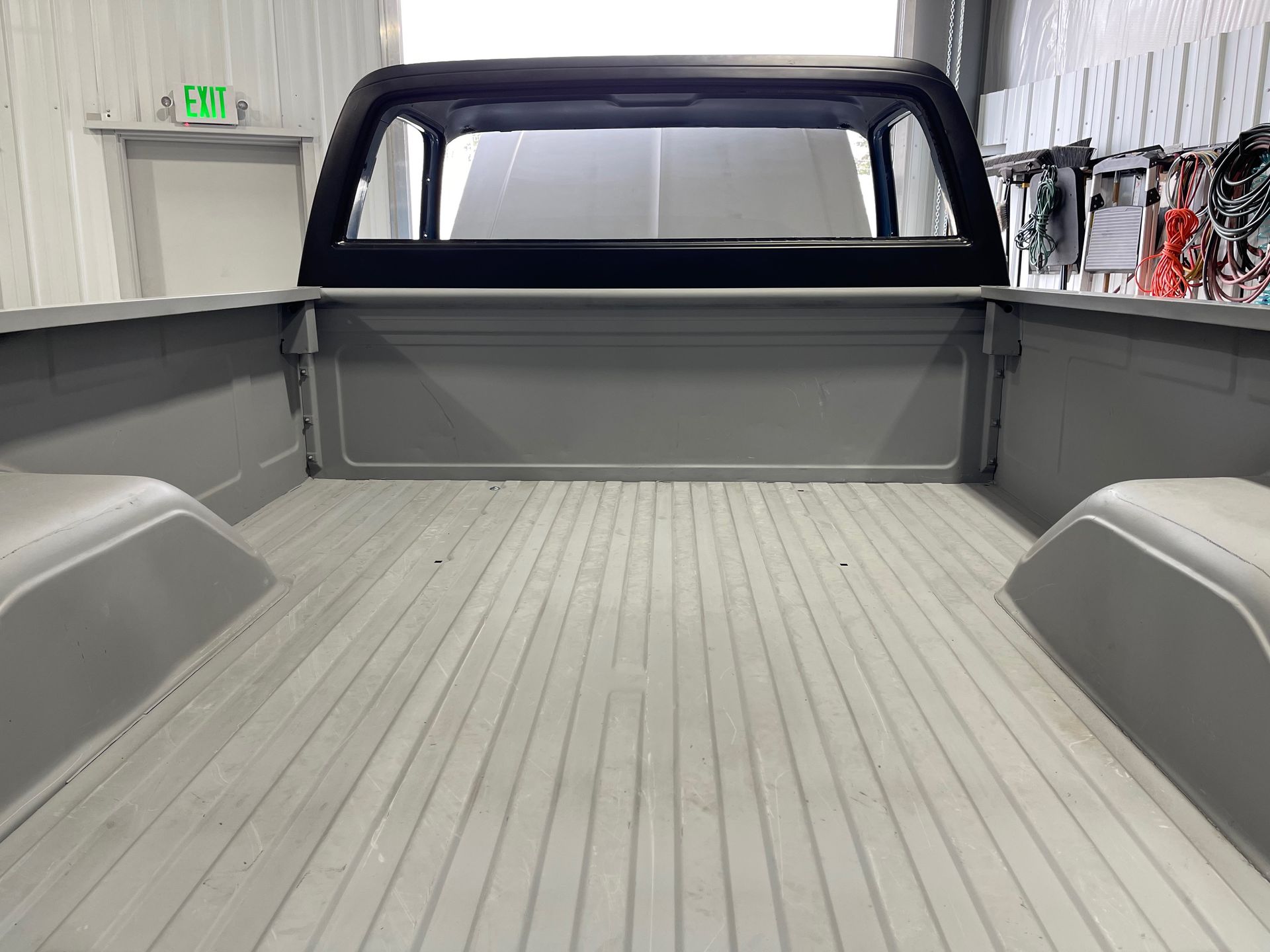 Empty pickup truck bed with a gray liner, viewed from the rear inside a garage.