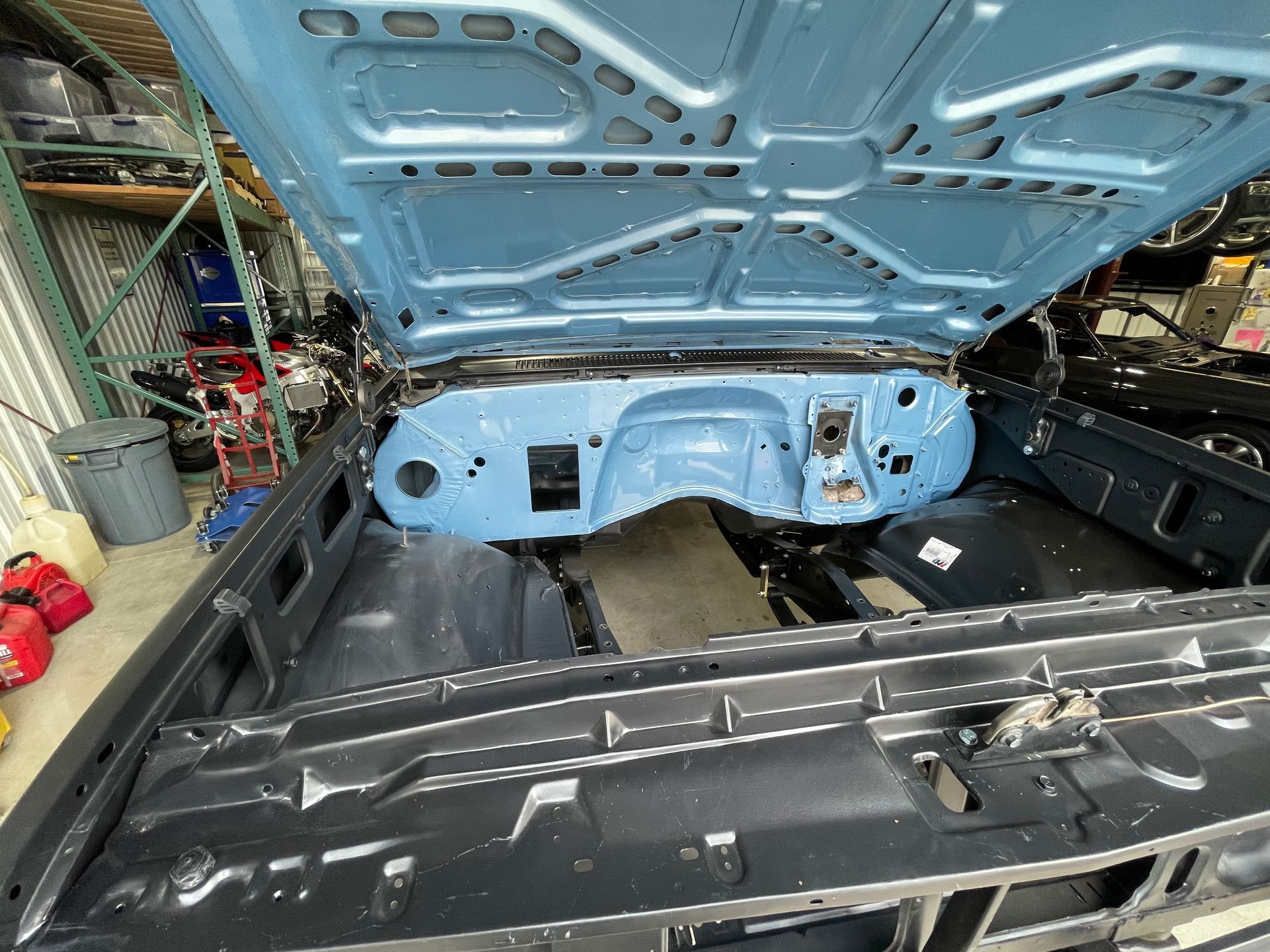 Classic car trunk interior with light blue metal body panels and open hood in a garage.