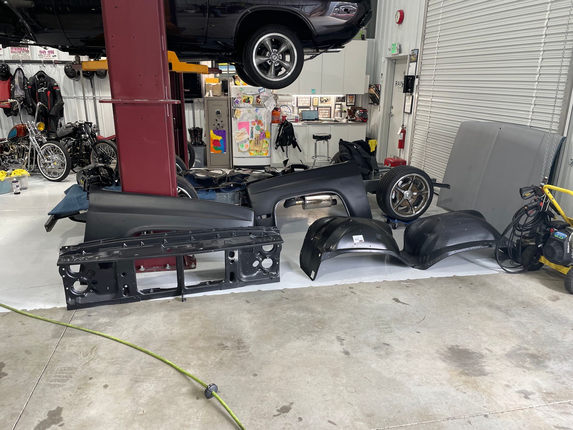 Auto shop floor with car body panels and parts laid out under a lifted vehicle