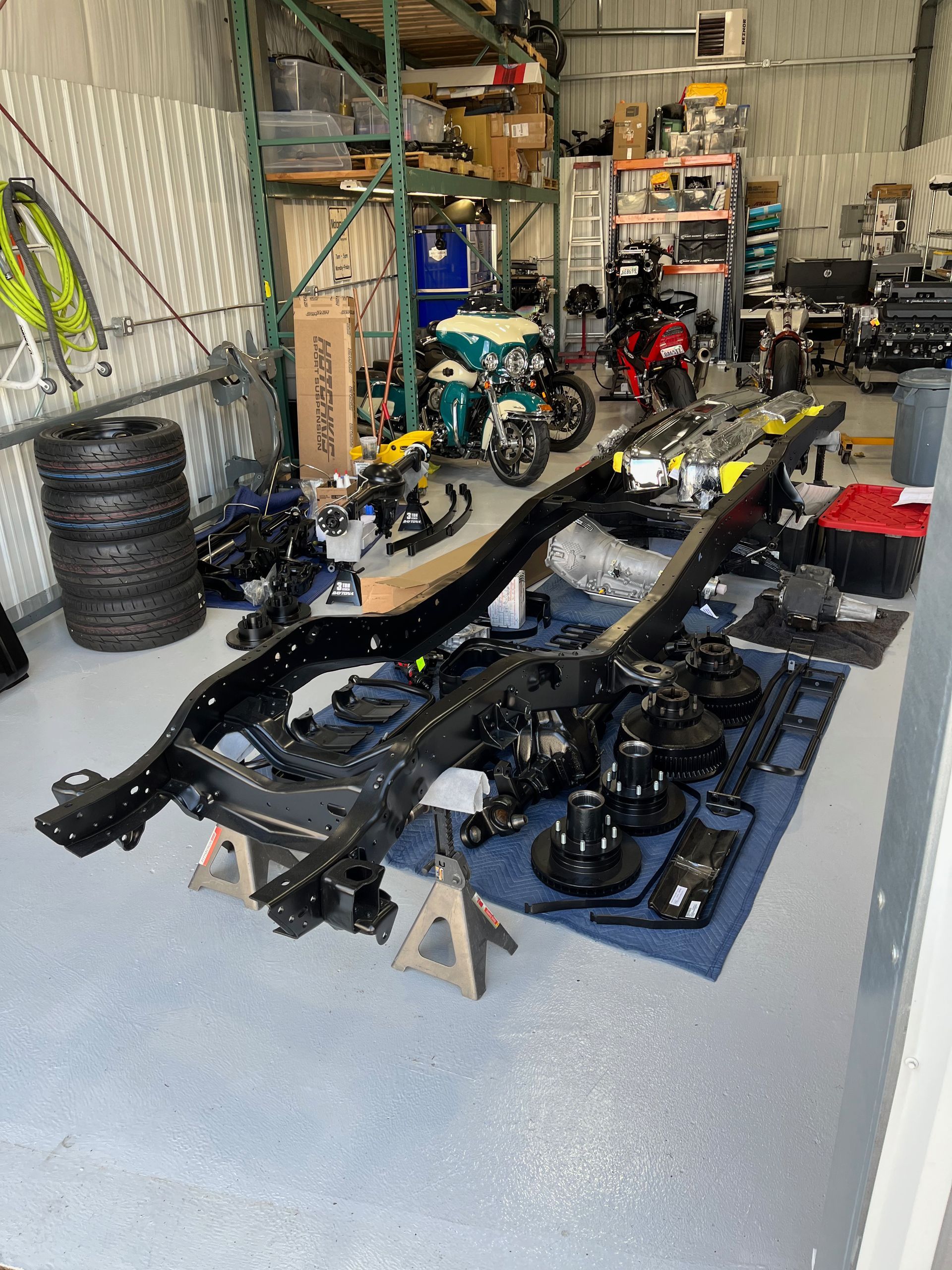 Auto parts and chassis frames laid out on the floor of a cluttered garage workshop
