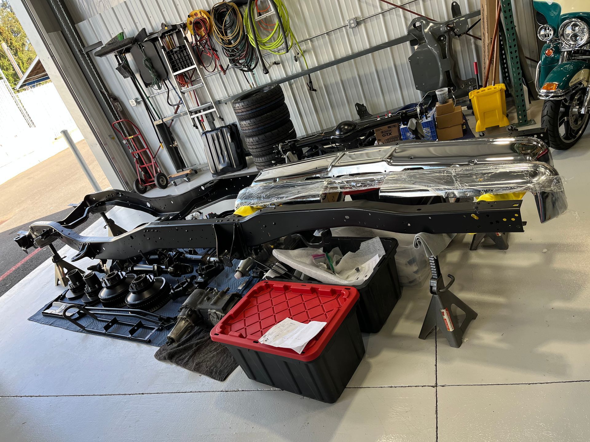 Car bumper parts laid out on garage floor beside trays and tools in a workshop.