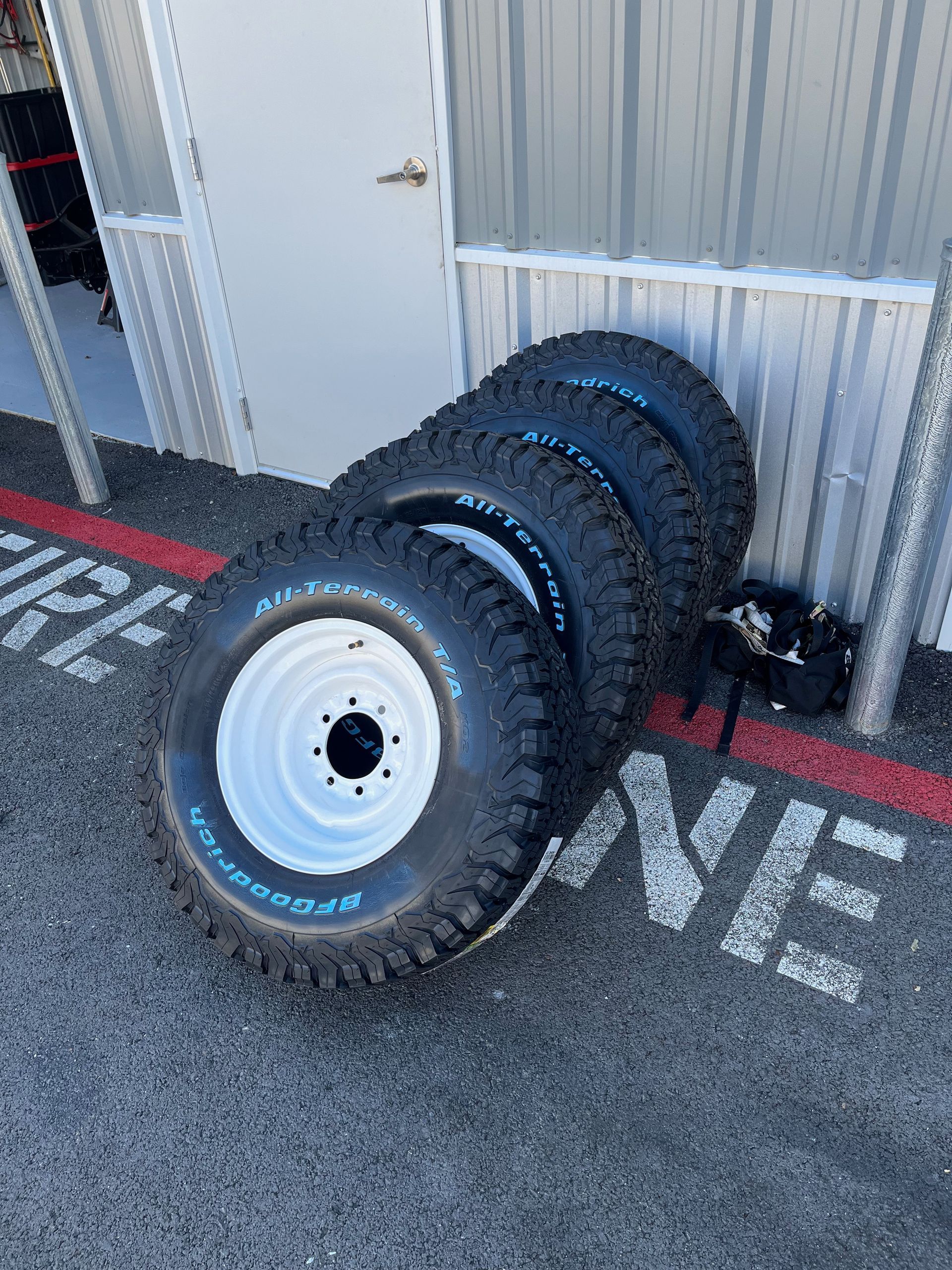 Stacked rugged off-road tires beside a white door on a gray concrete floor.