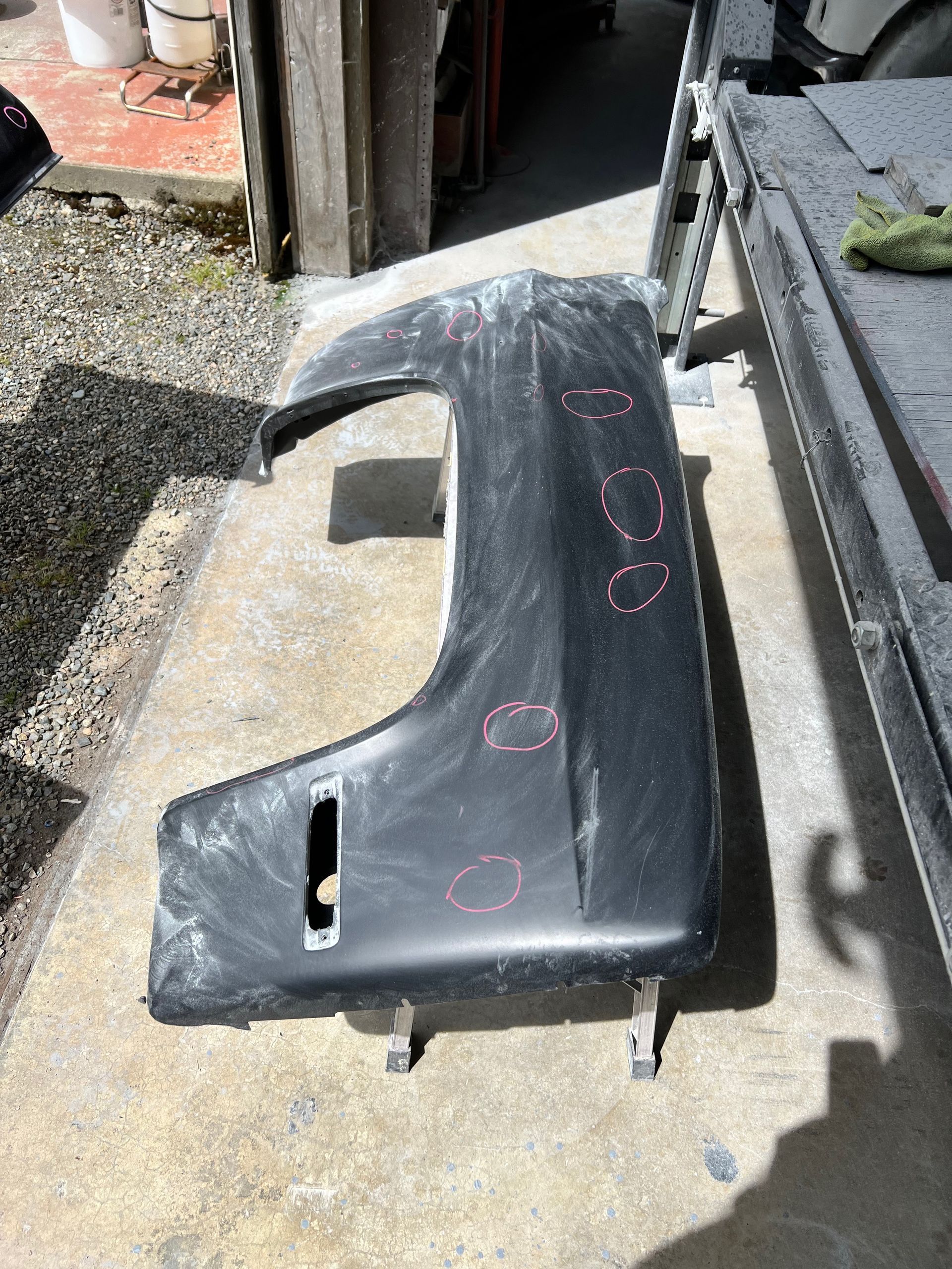 Black car interior door panel on the ground outdoors, with pink chalk markings and cutouts