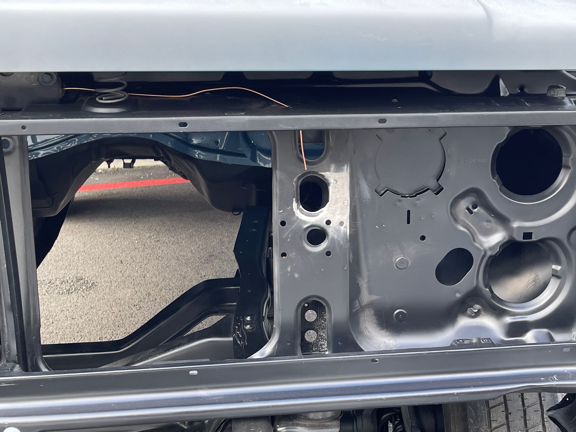 Close-up of a car’s exposed rear body panel with missing trim and visible openings in gray metal.