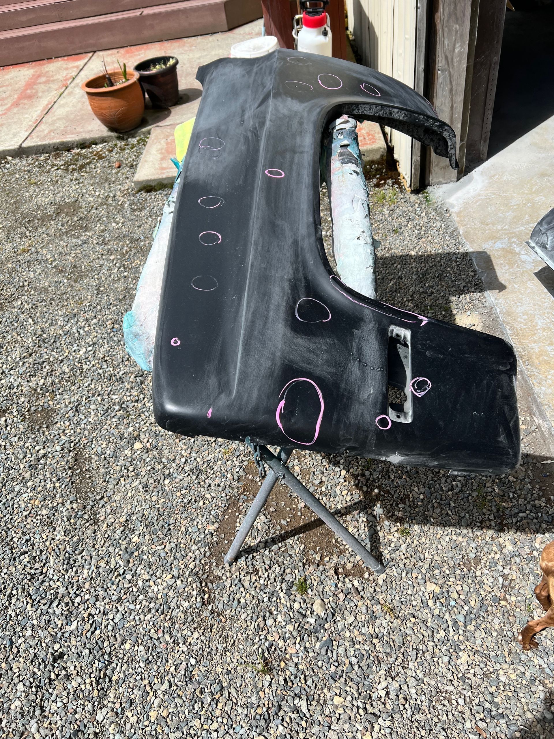 Black car body panel on a stand outdoors, with chalk marks and a cut-out opening.