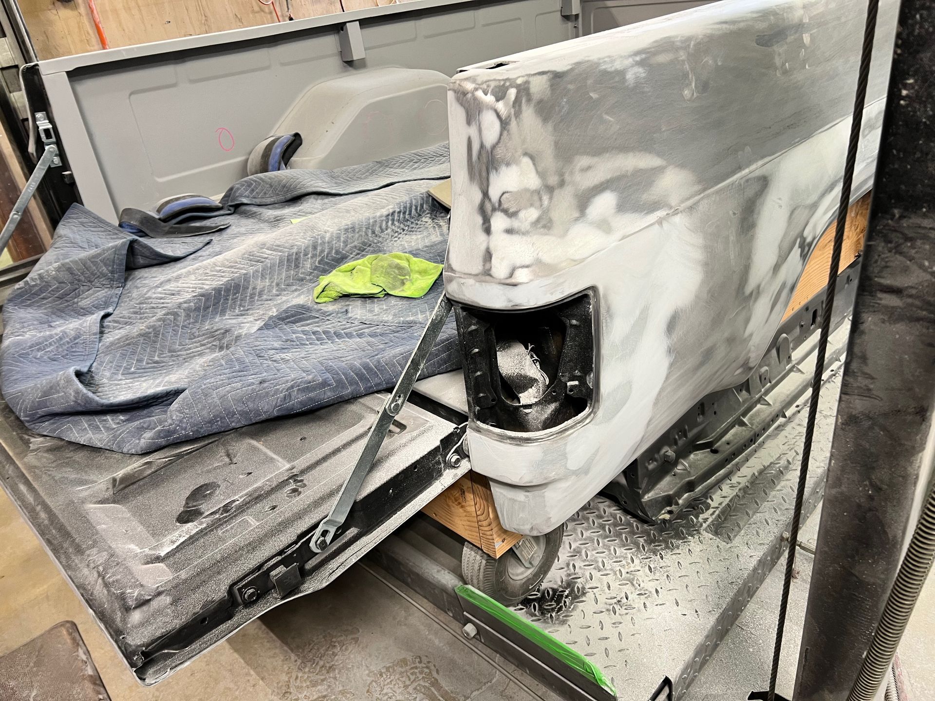 Auto body panel being repaired, with gray primer, sanding marks, and a detached taillight area.