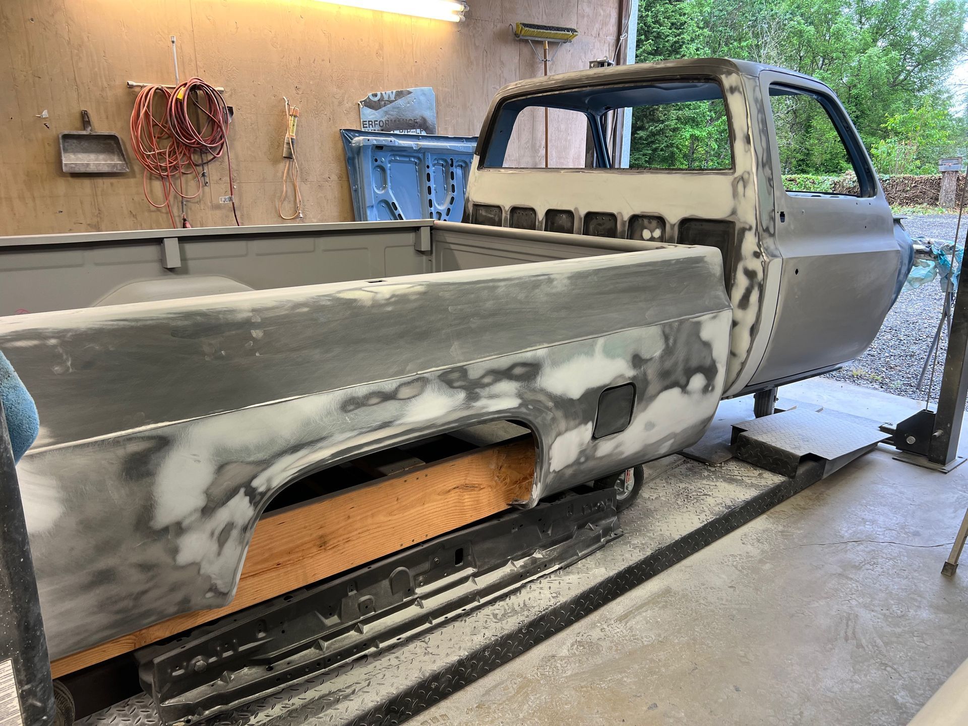 Partially restored pickup truck bed in a garage, with primer and body filler visible.