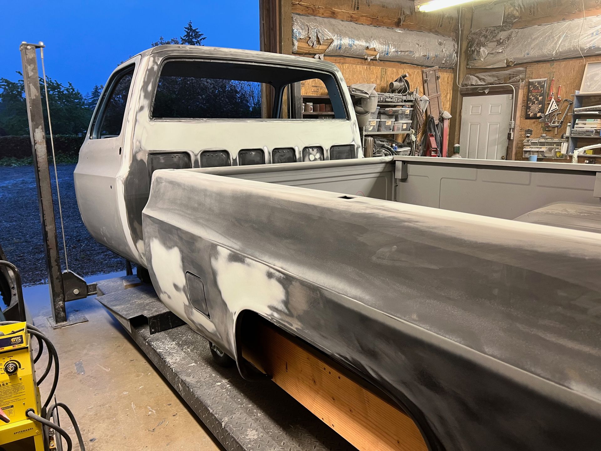 Primered pickup truck bed in a garage, with bodywork in progress and sanding dust visible.
