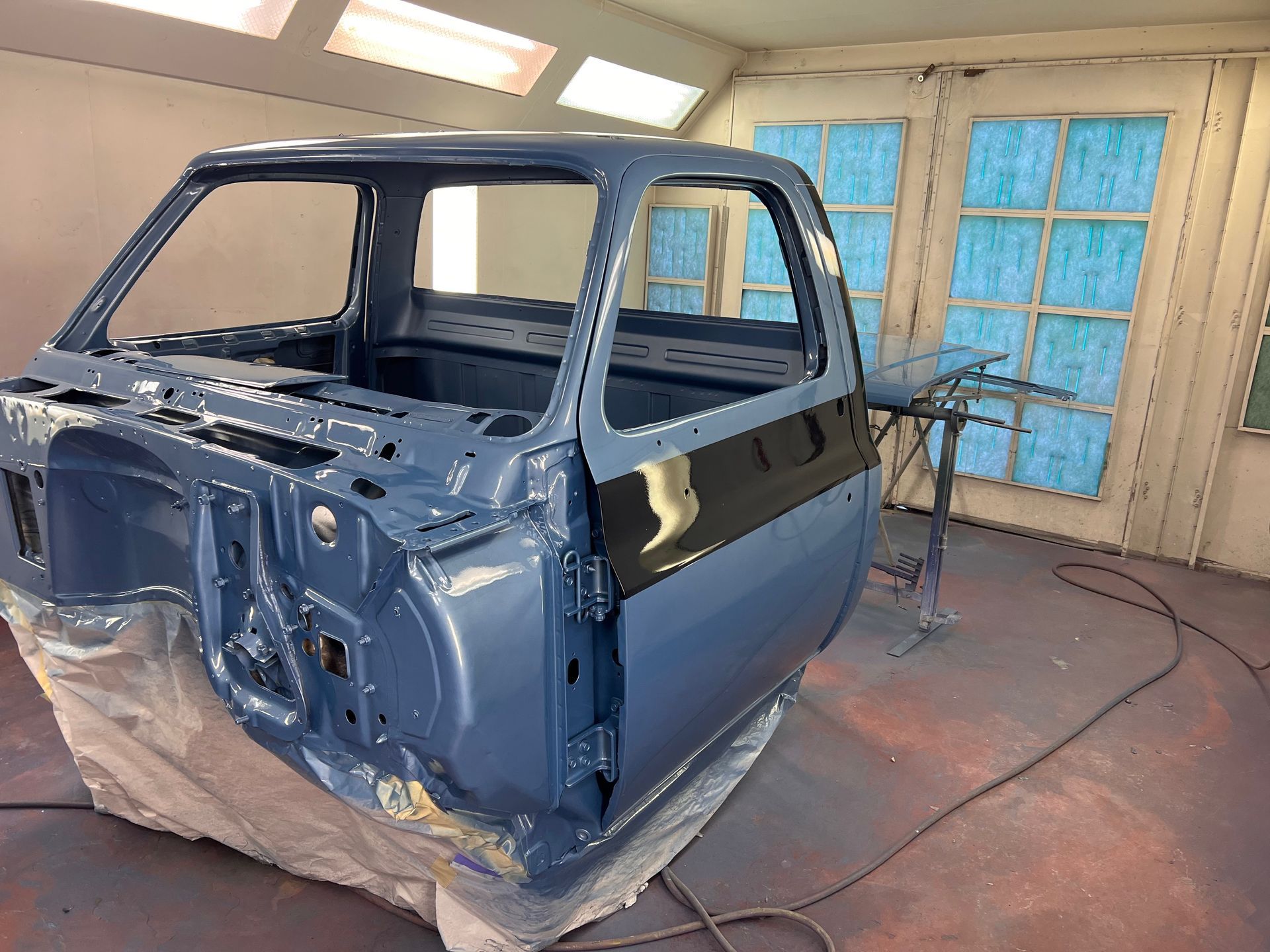 Blue car body in a workshop, masked for painting and surrounded by sanding dust and garage doors