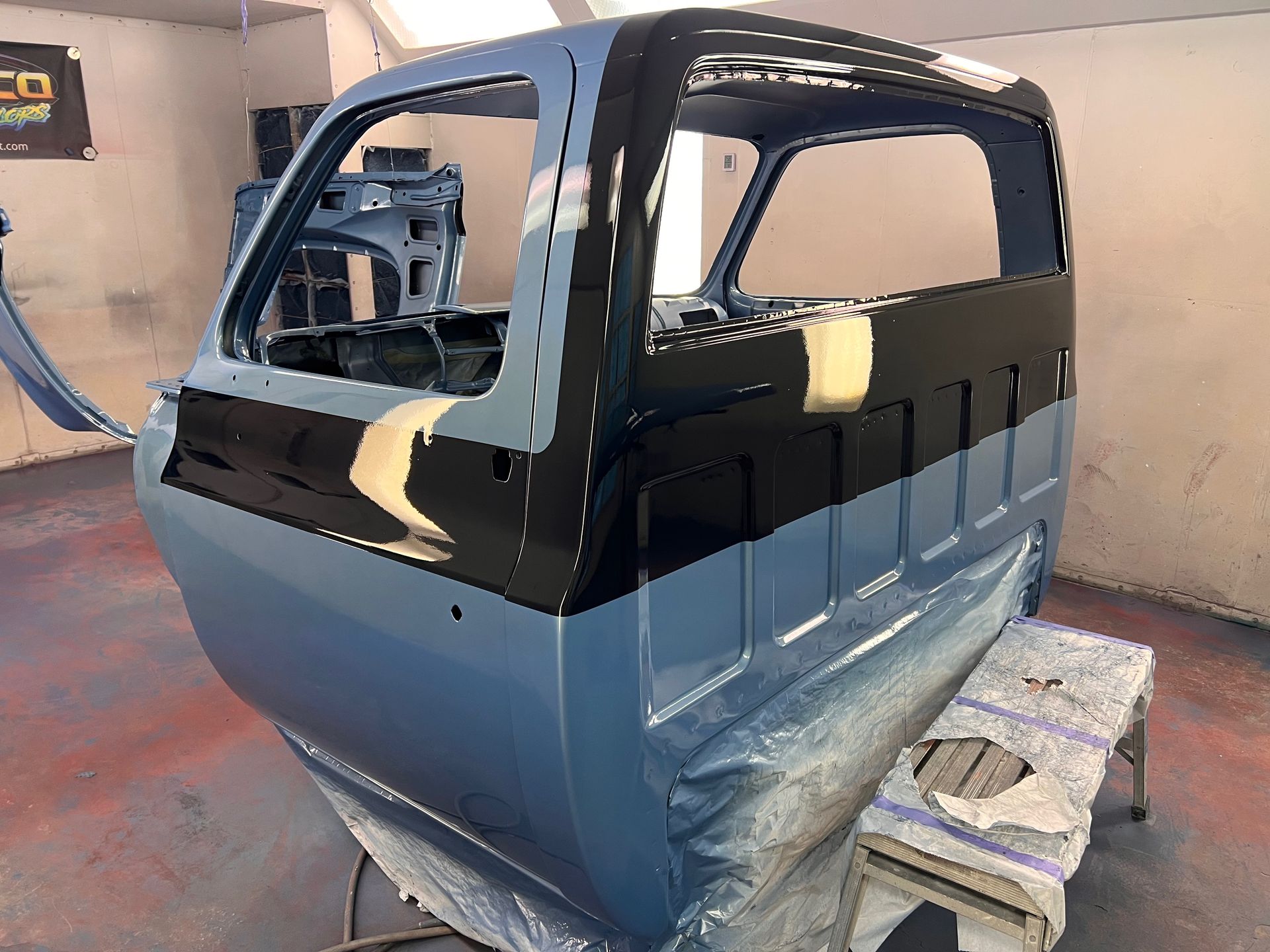 Two-tone car body shell in a workshop, black and blue-gray, resting on blocks with windows removed