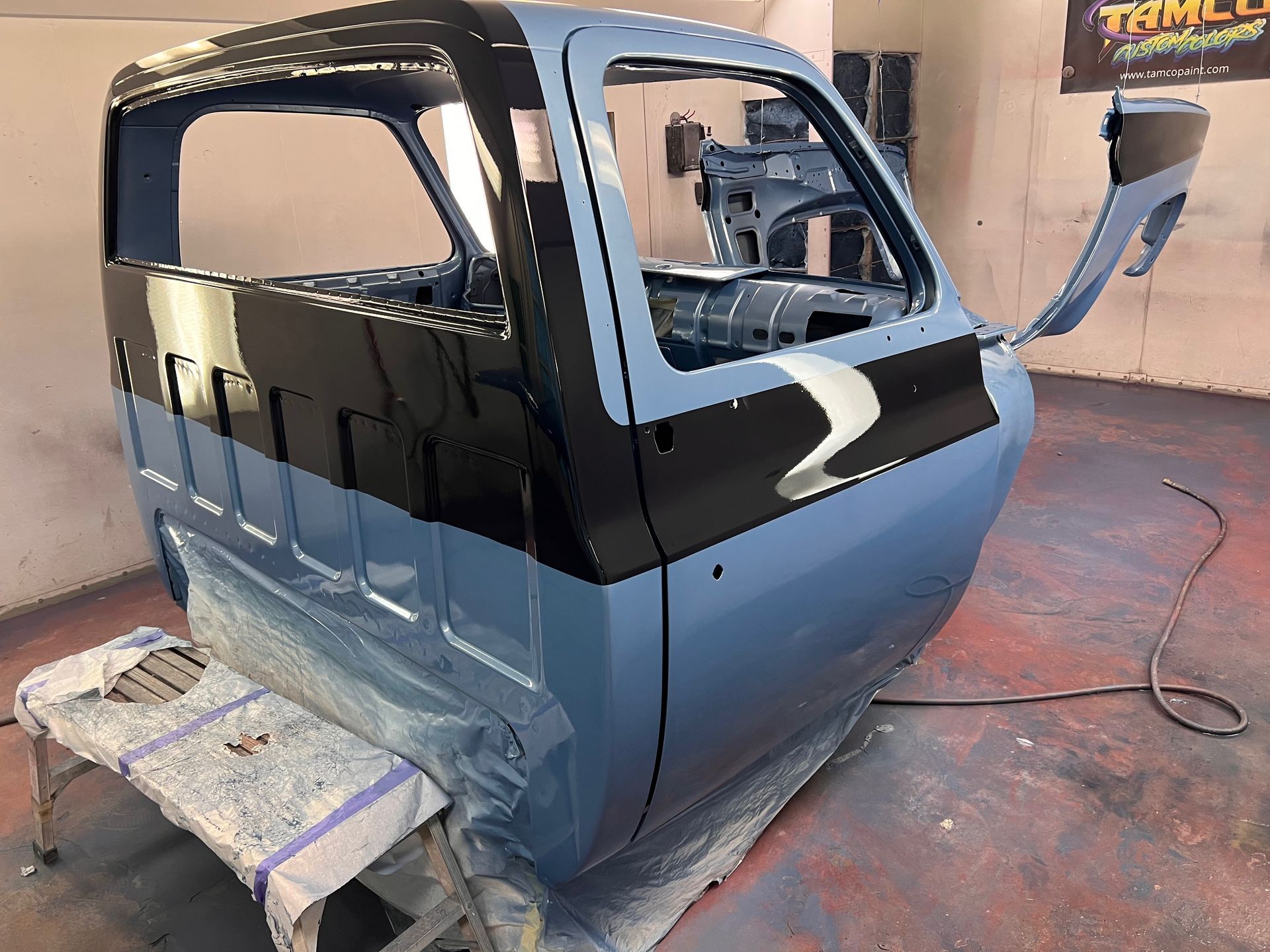 Partially painted blue and black car body in a workshop, with windows and door openings visible