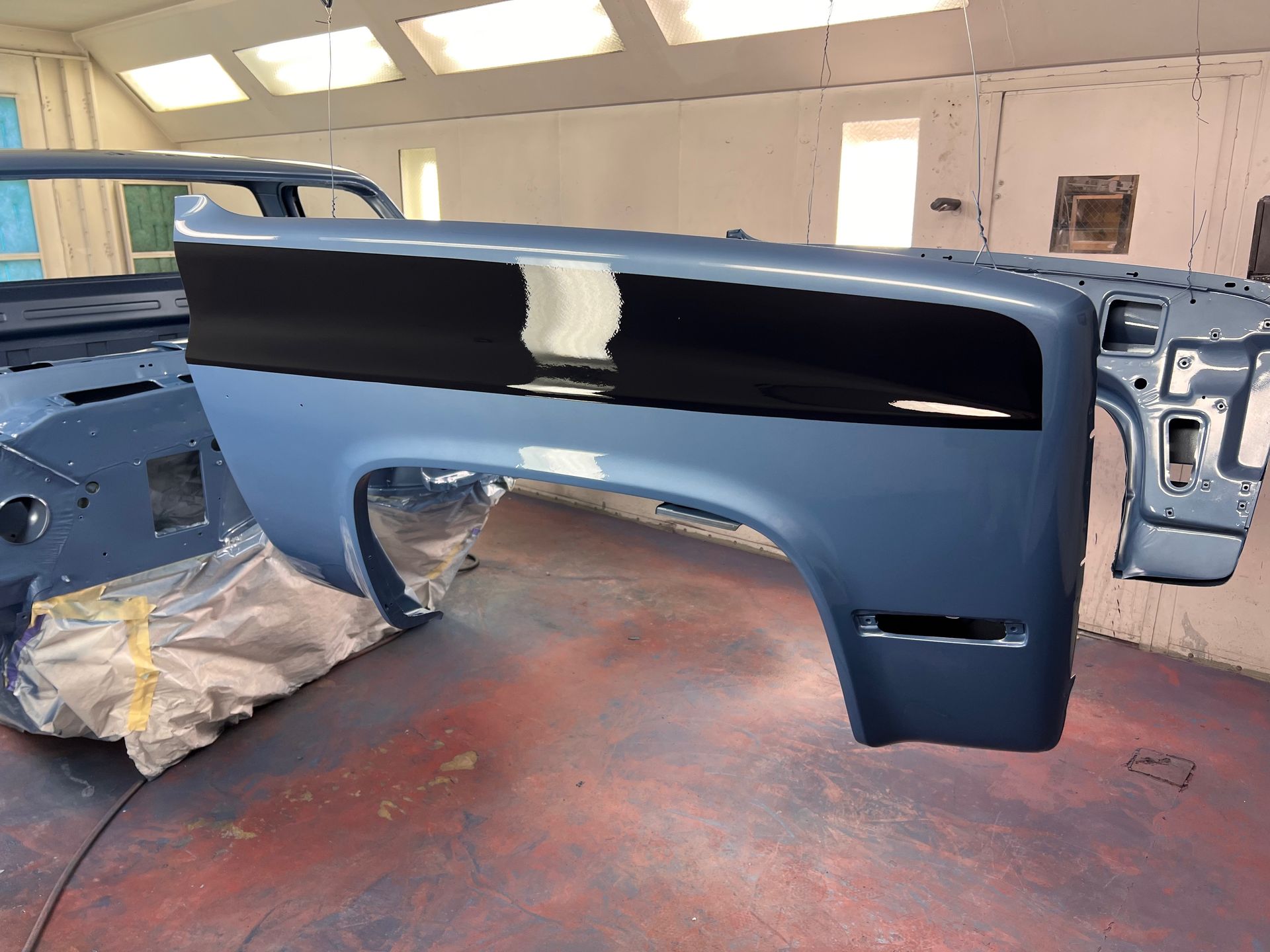 Painted car front panel in a workshop, blue-gray with a glossy black top section.