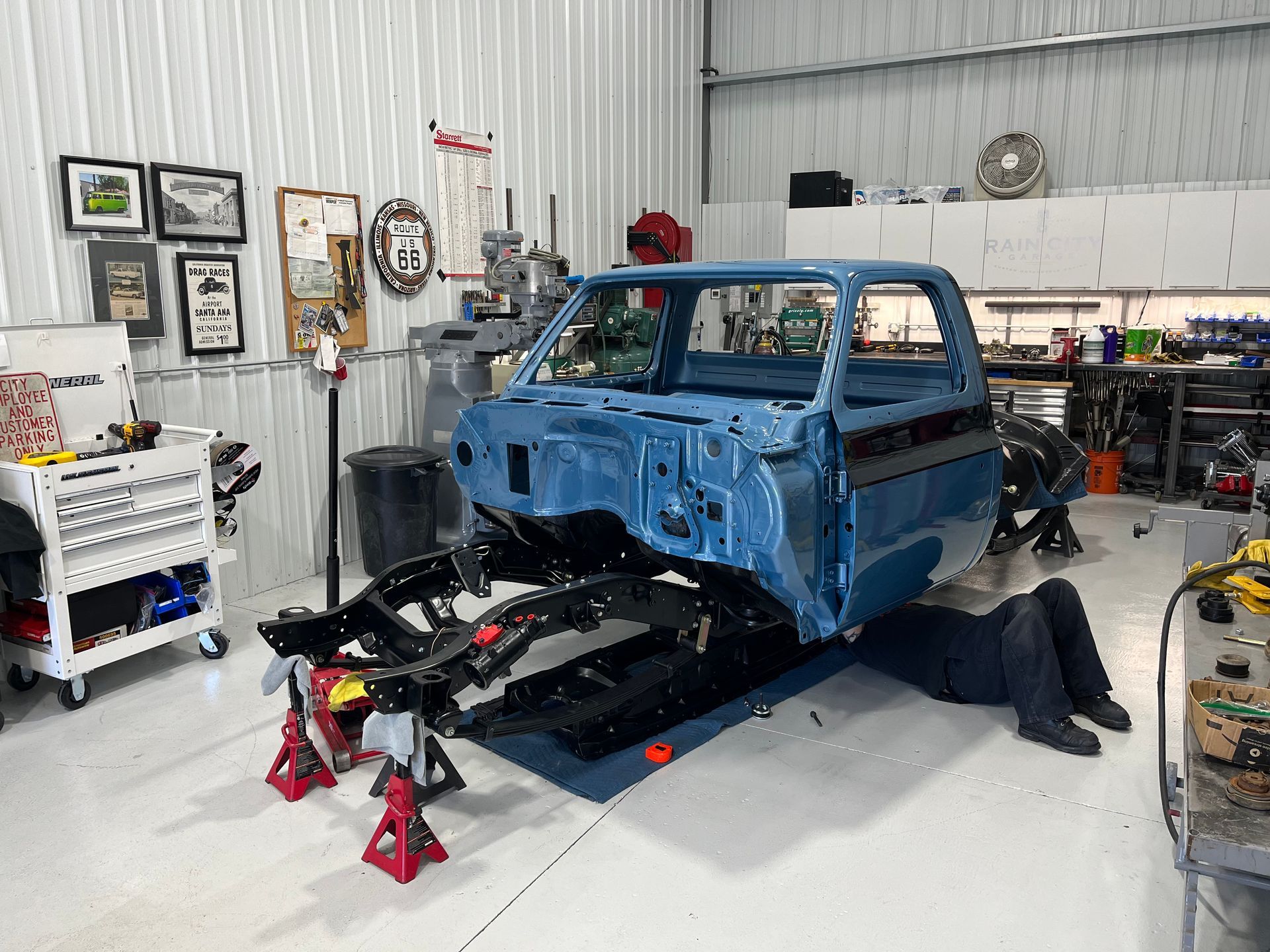 Blue classic truck body on jack stands in a garage, mid-restoration with exposed chassis and tools around it
