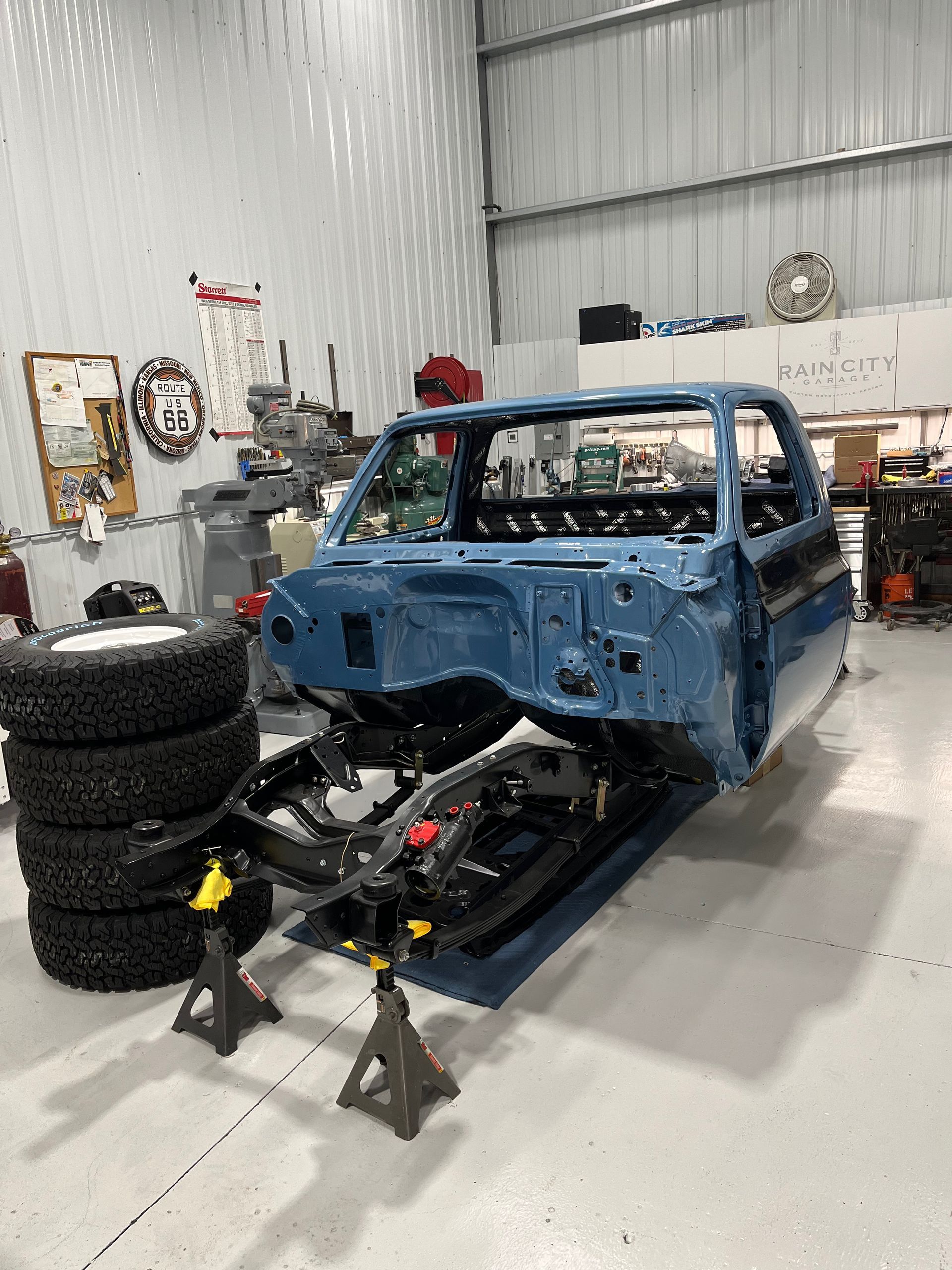Blue car body shell on jack stands in an auto workshop, with the front suspension removed.