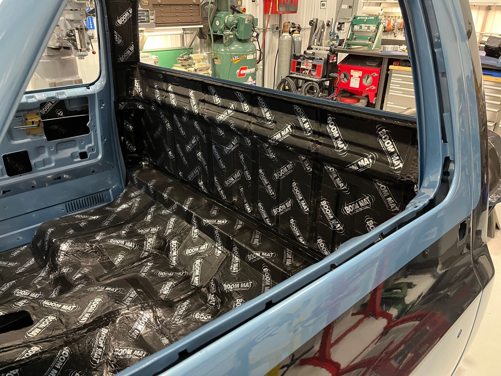 Car interior lined with black sound-deadening material, viewed through an open side door.