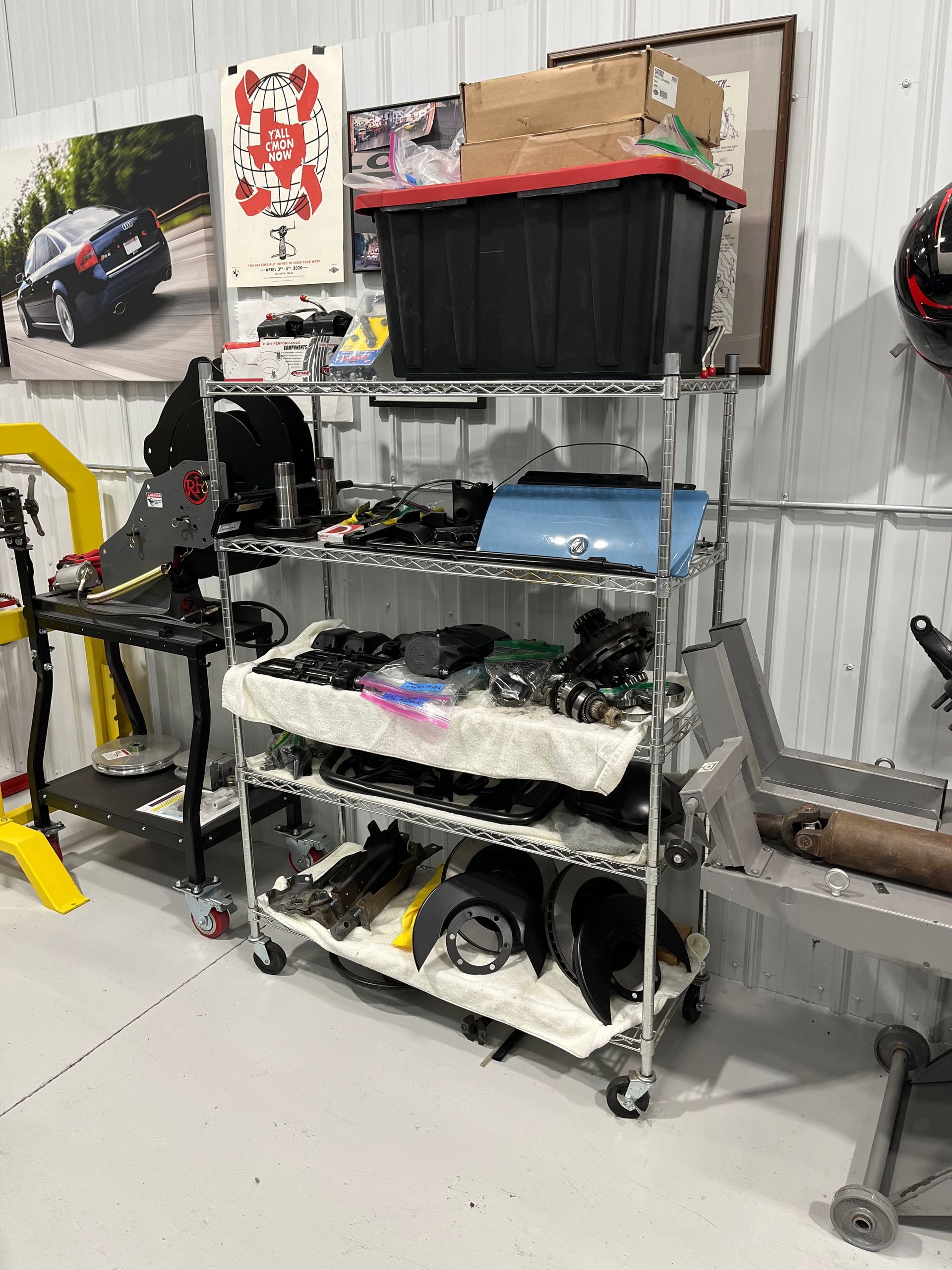 Shelving with electronics and tools in a workshop, including a monitor and cables against a metal wall.