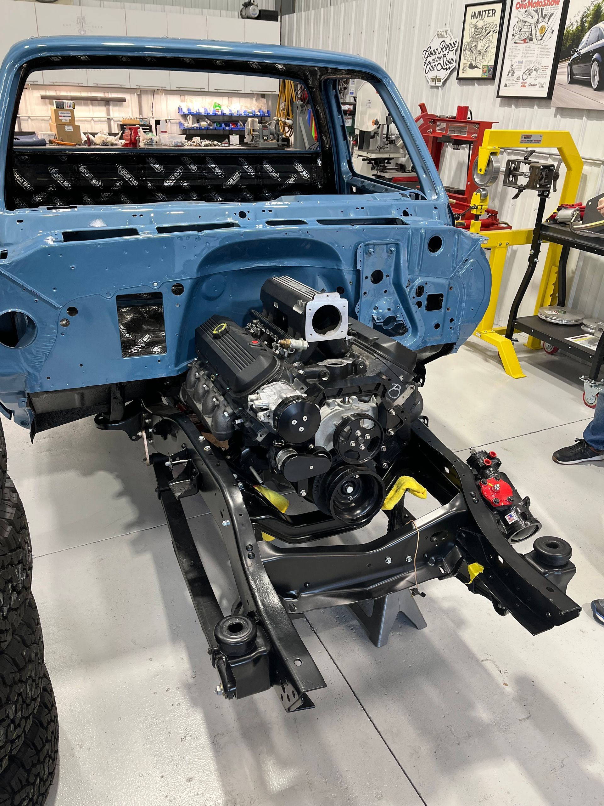 Blue car body shell in a workshop with the engine and chassis exposed on a rolling frame