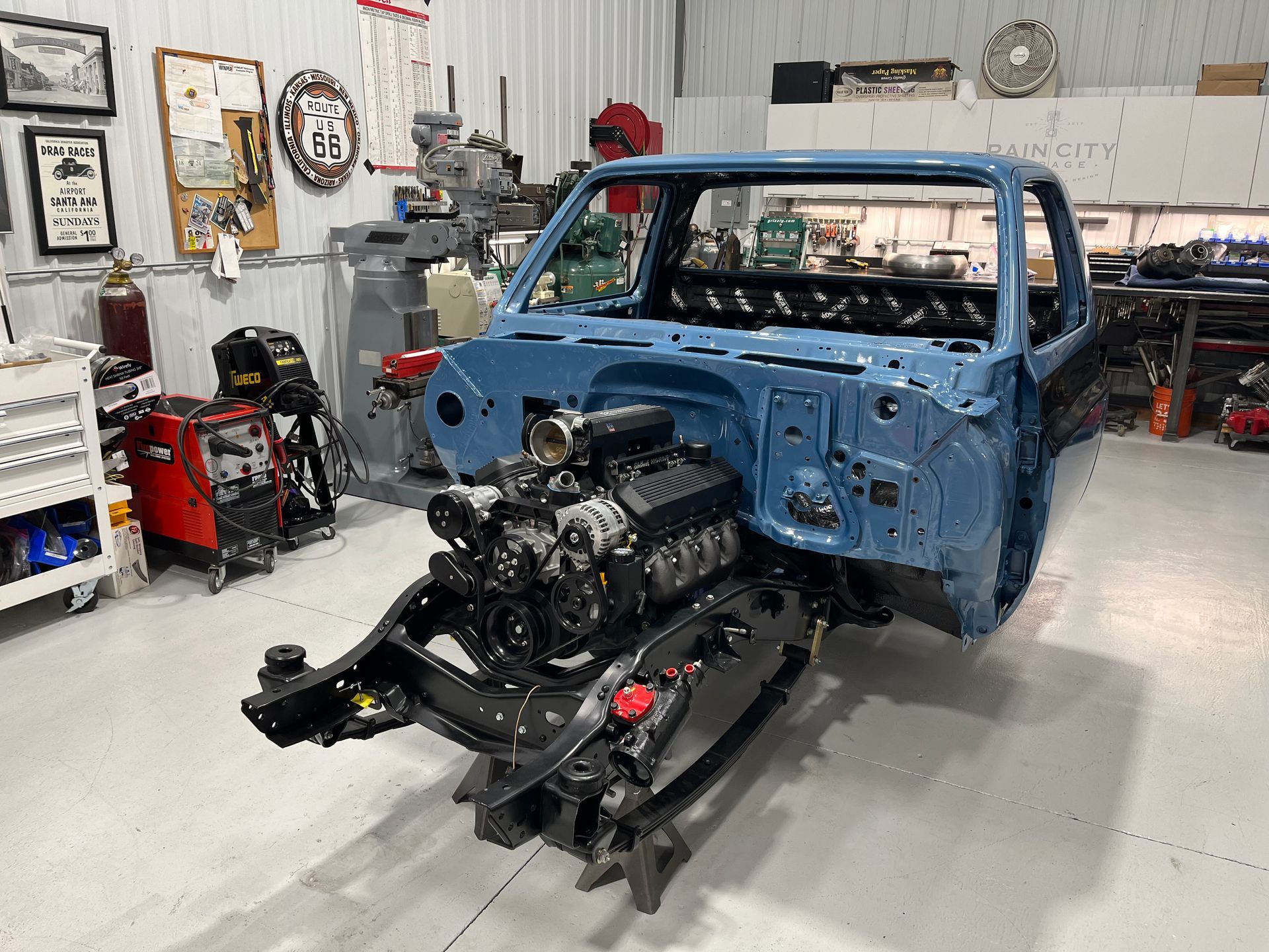 Blue truck body with exposed engine and chassis in a workshop garage