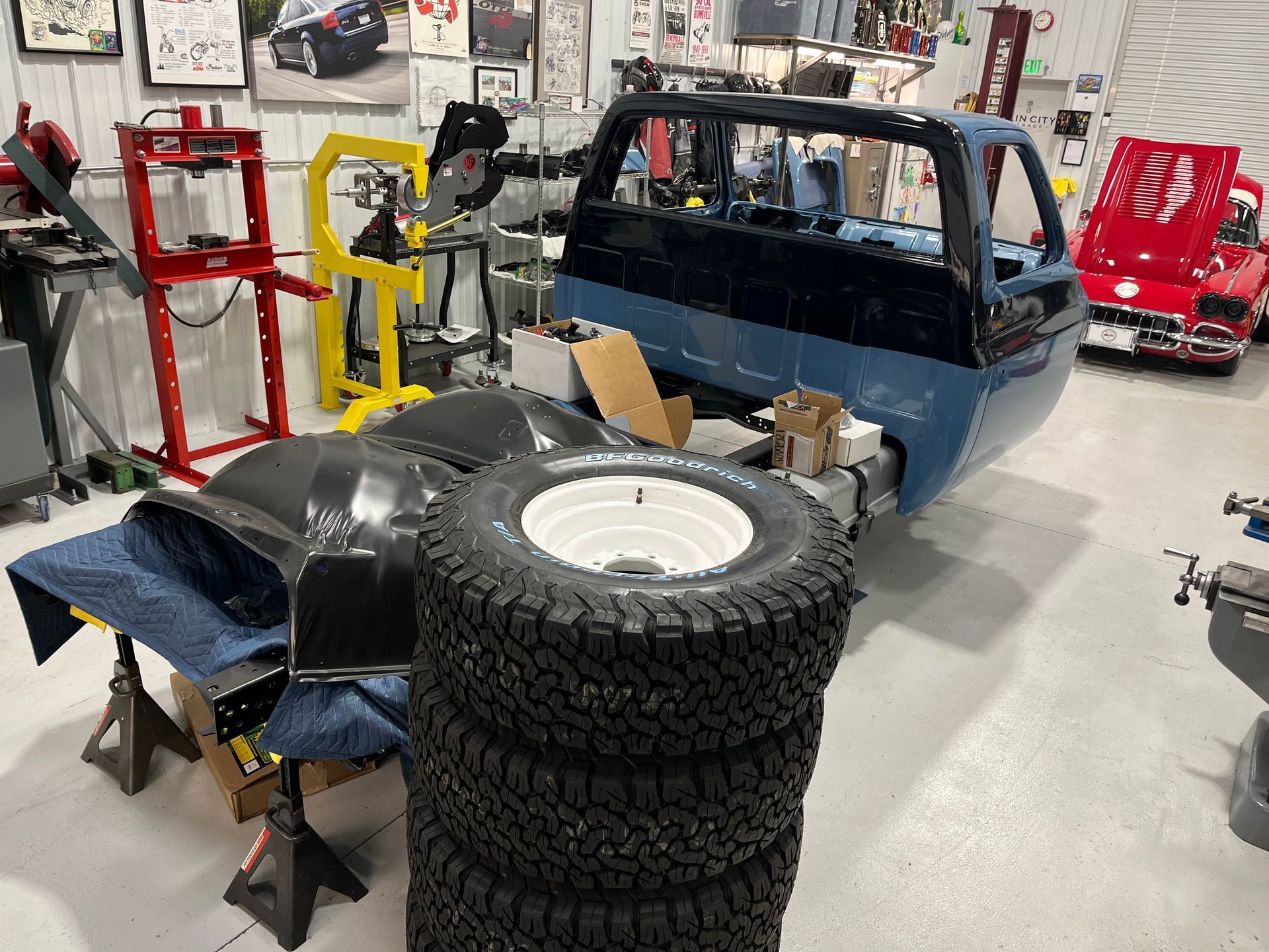 Blue off-road vehicle in a workshop with stacked tires and tools around it