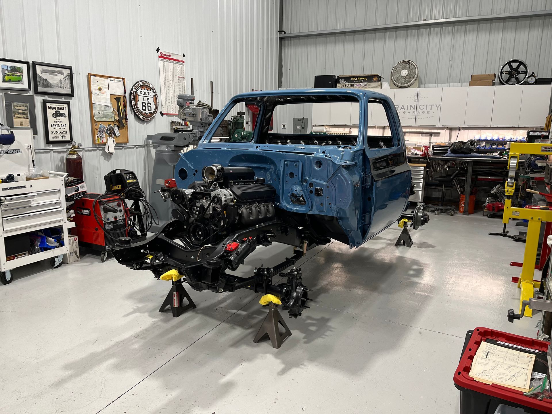 Blue truck body on jack stands in an auto shop, with the front end removed during repair.