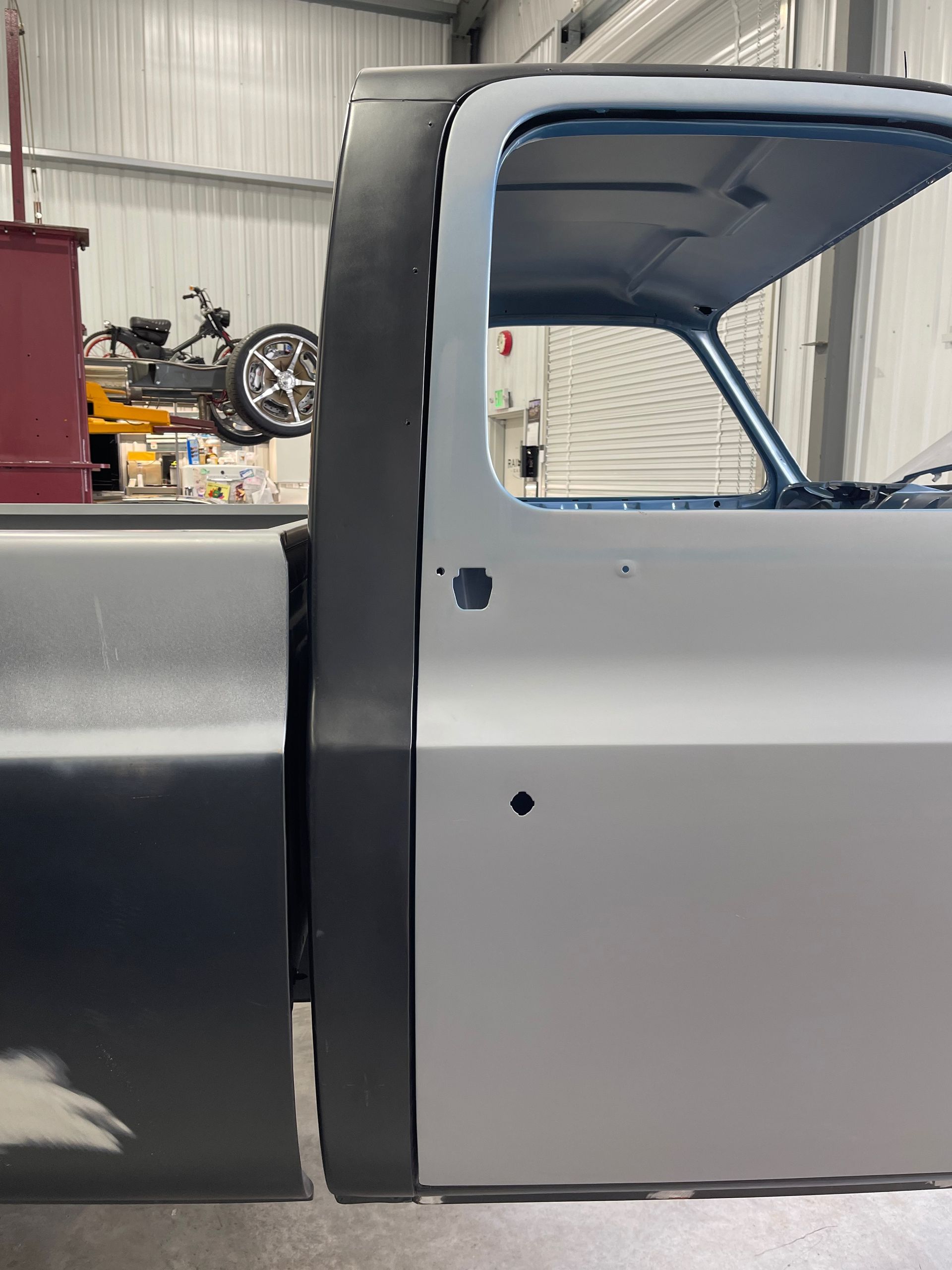 Two-tone gray classic car body in a workshop, showing the side door opening and black trim seal