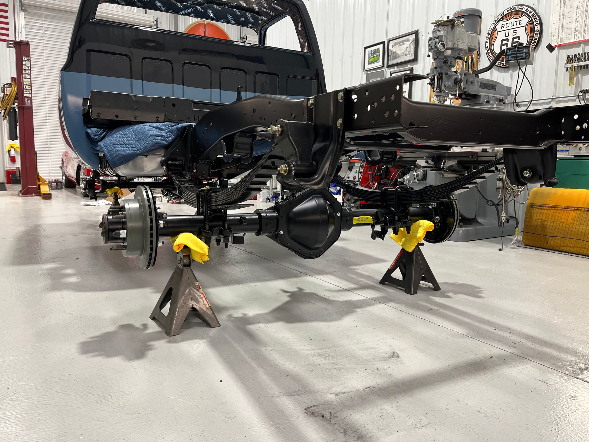 Vehicle frame on jack stands inside a garage, with wheels removed and tools nearby.