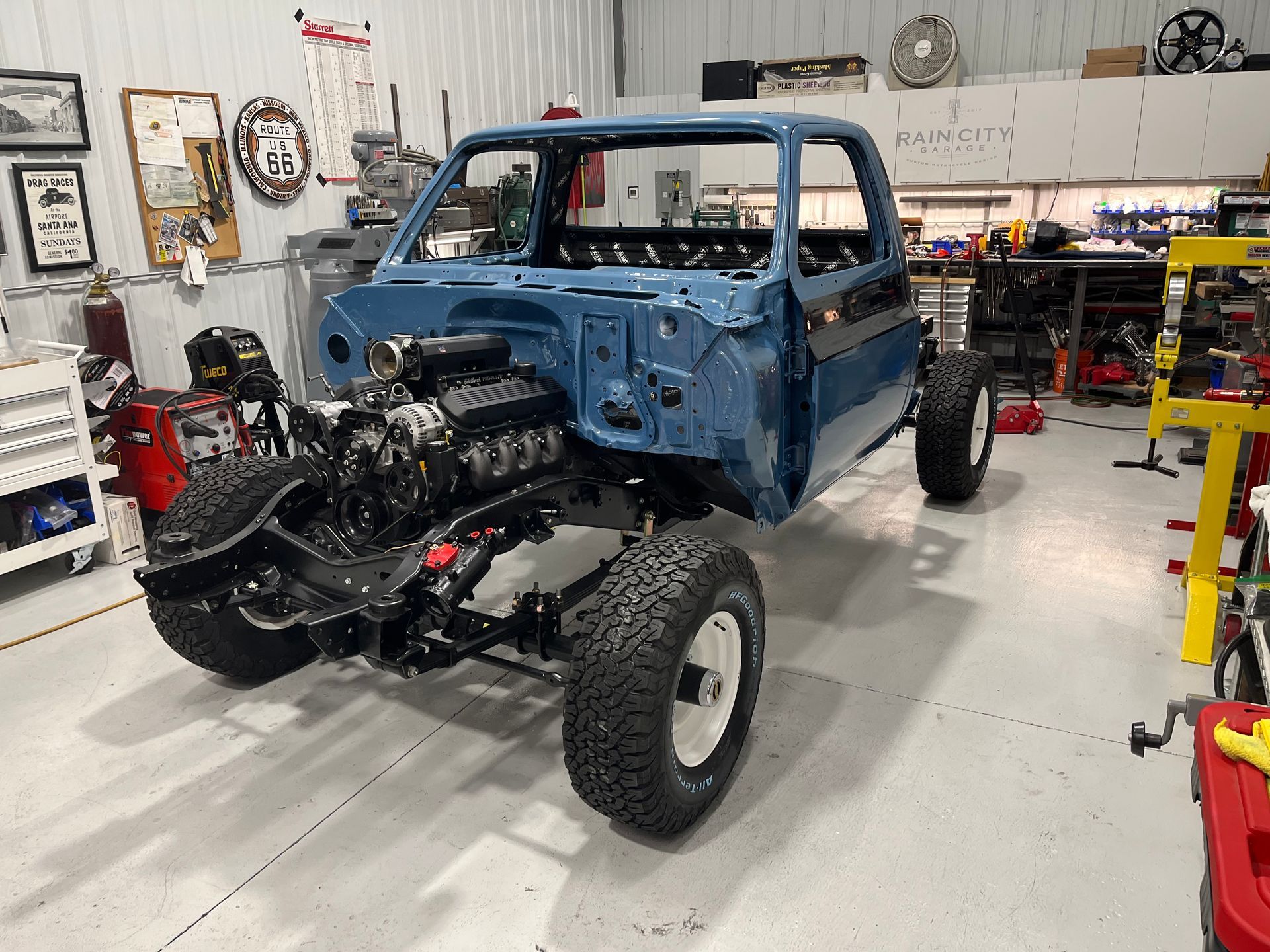 Blue pickup truck under restoration in a workshop, with exposed engine and no front body panels