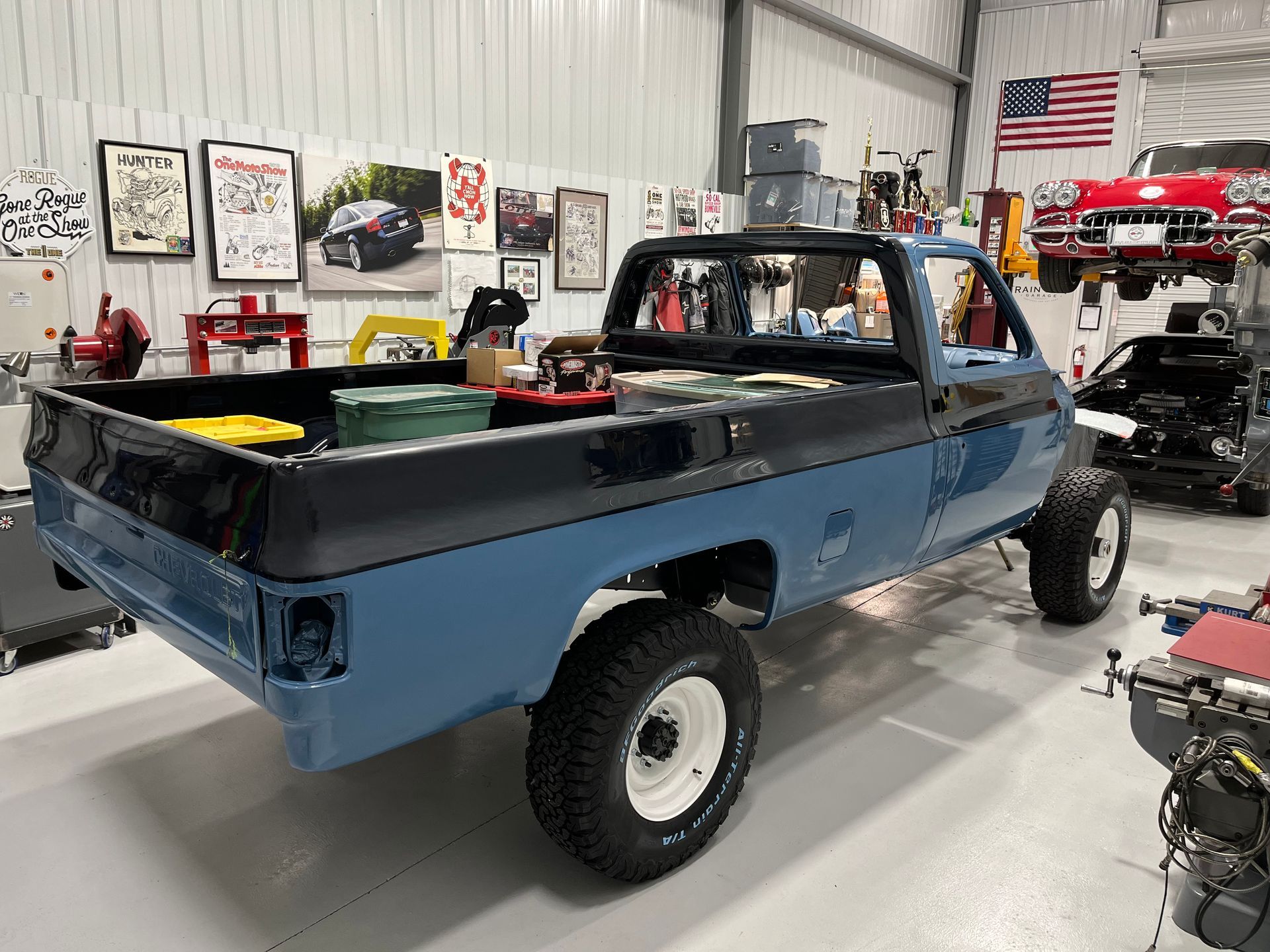 Blue pickup truck in a workshop garage, viewed from the rear-left side