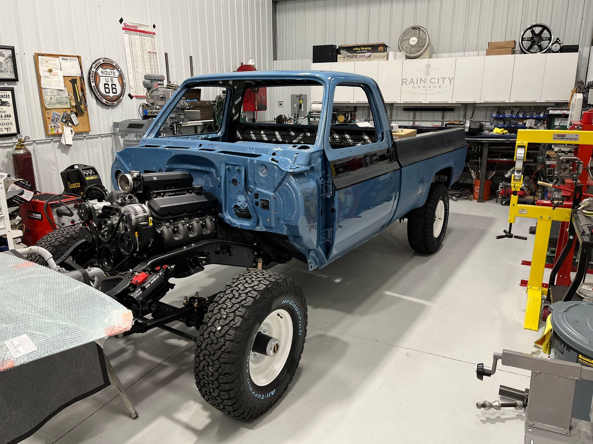 Blue classic pickup truck in a garage, undergoing restoration with front engine exposed