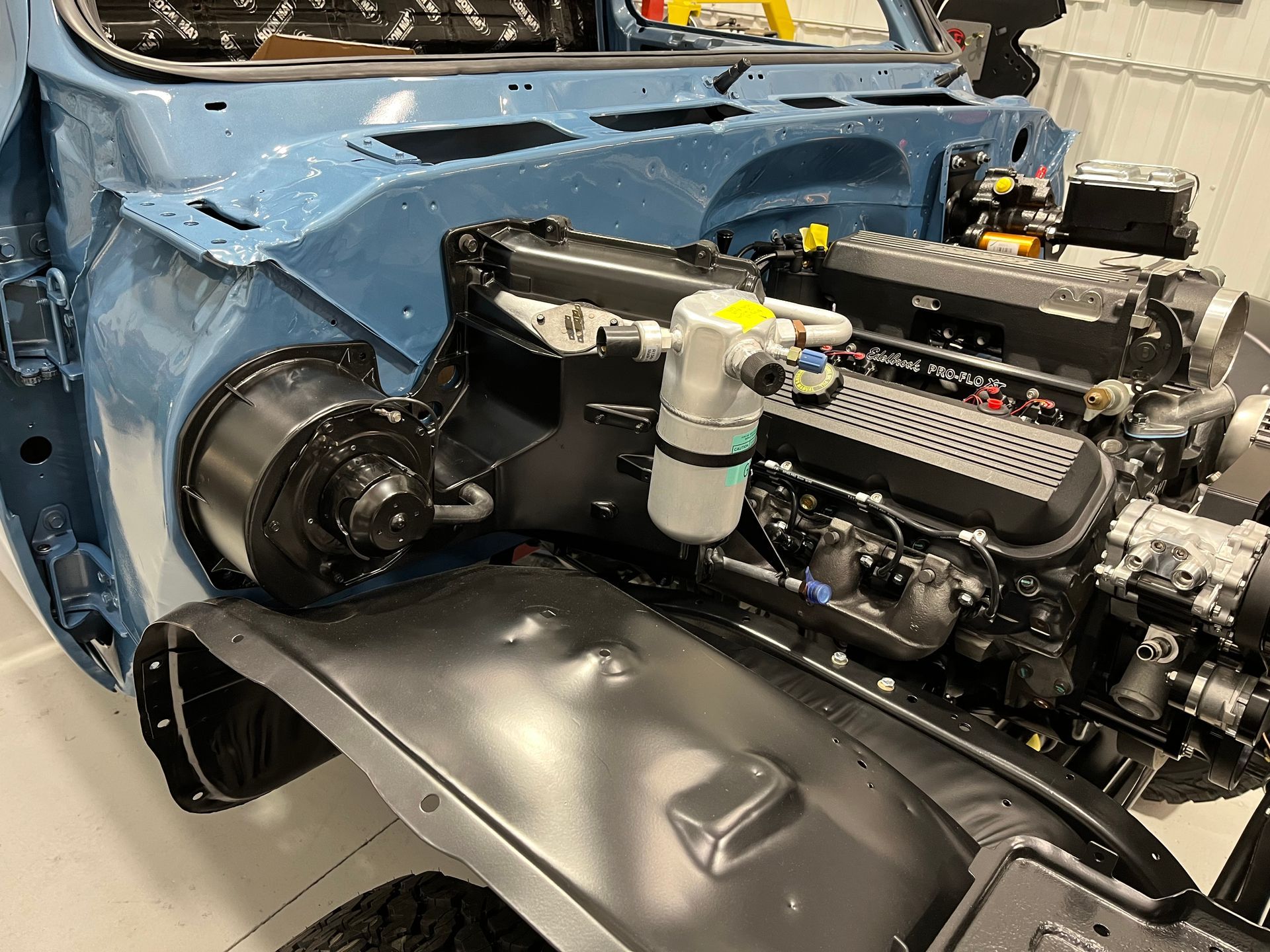 Blue car with front body panels removed, exposing the engine bay in a workshop