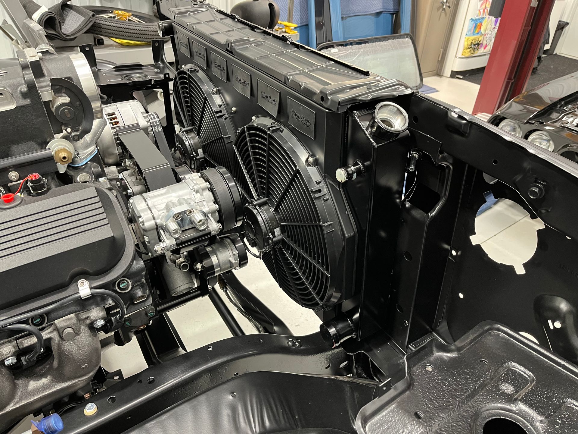 Car engine and radiator assembly in a workshop, with black fans and exposed front frame.