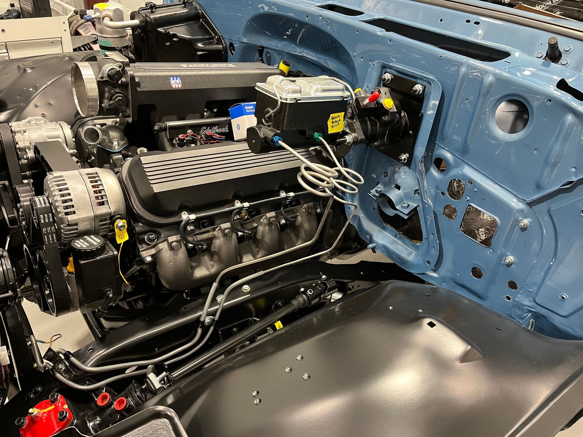 Partially assembled car engine bay with black engine, blue firewall, and exposed wiring